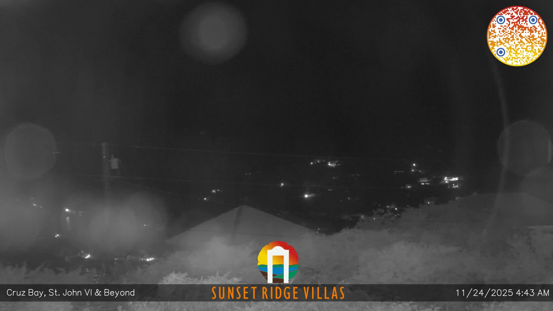 The image displays a dark, blurry nighttime outdoor scene of a distant landscape with scattered lights, significantly obscured by rain or condensation on the camera lens.