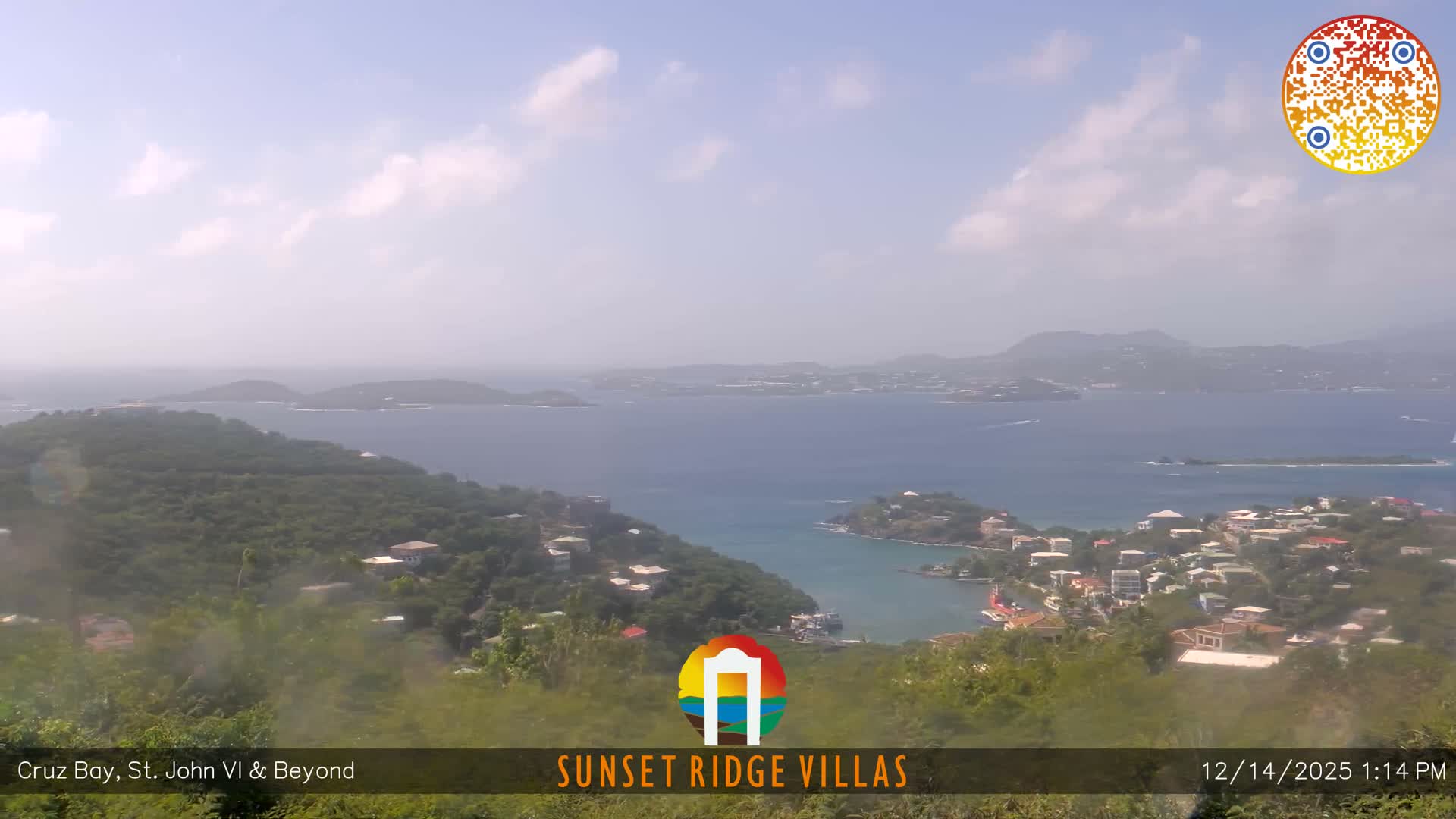 A sweeping nighttime vista reveals a densely lit coastal town sprawling across hillsides that descend to a dark bay, with distant landmasses faintly visible under an overcast sky.
