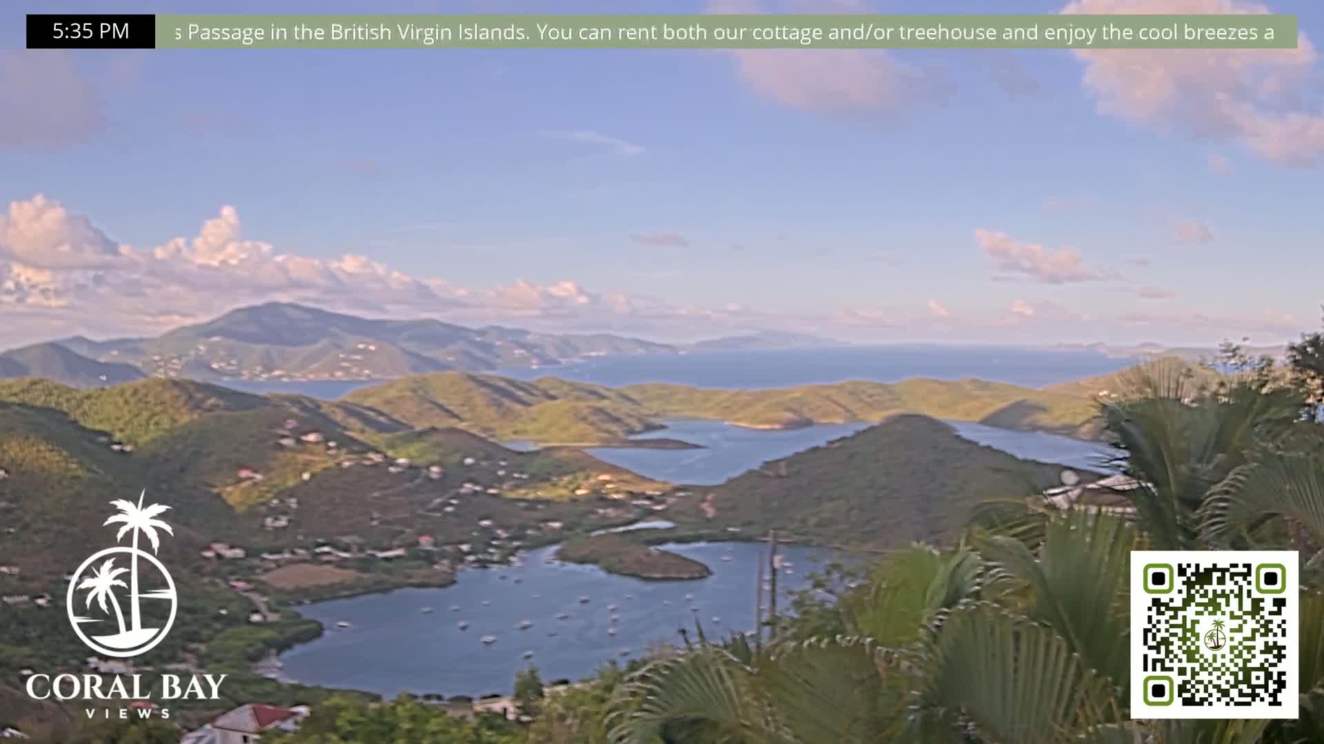 A partly cloudy afternoon view of a tropical bay surrounded by green hills and the ocean.