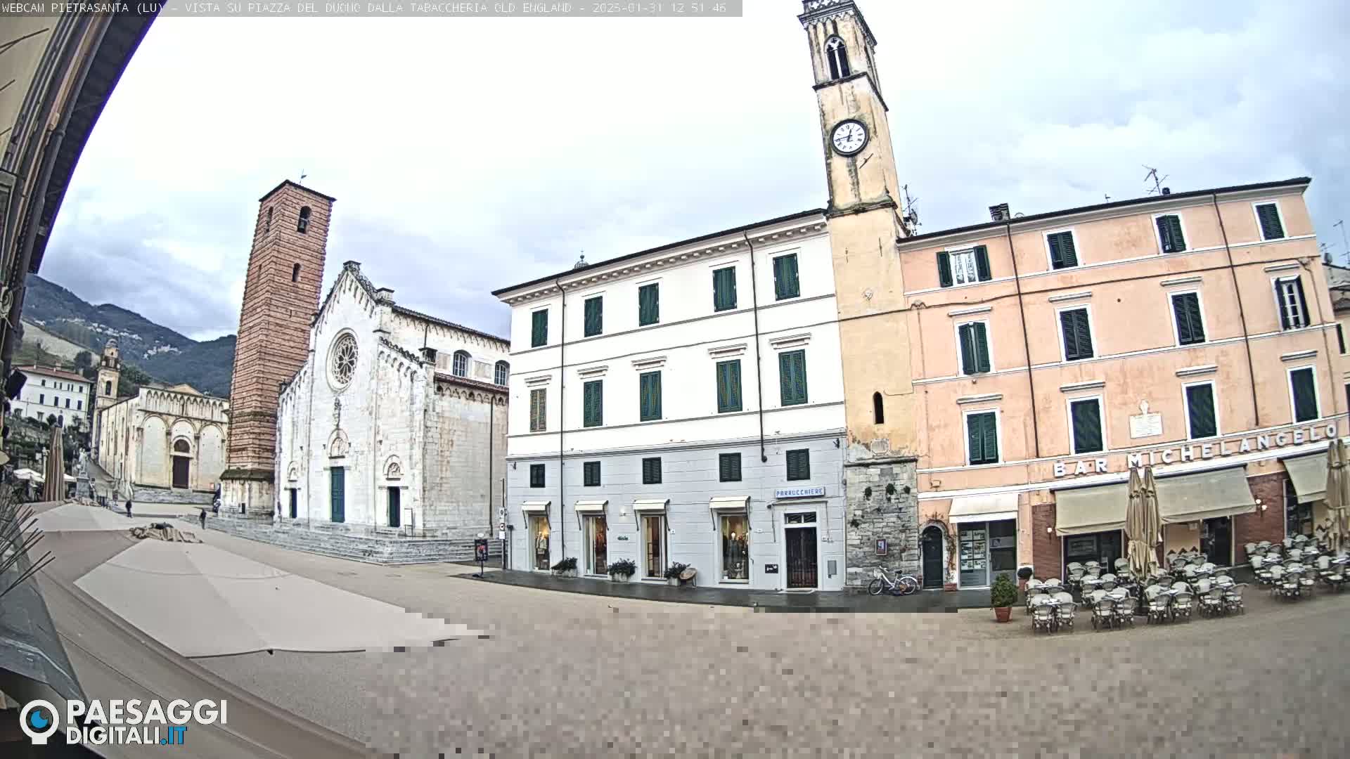 A town square is seen with buildings, including a church with a tall bell tower, under an overcast sky.