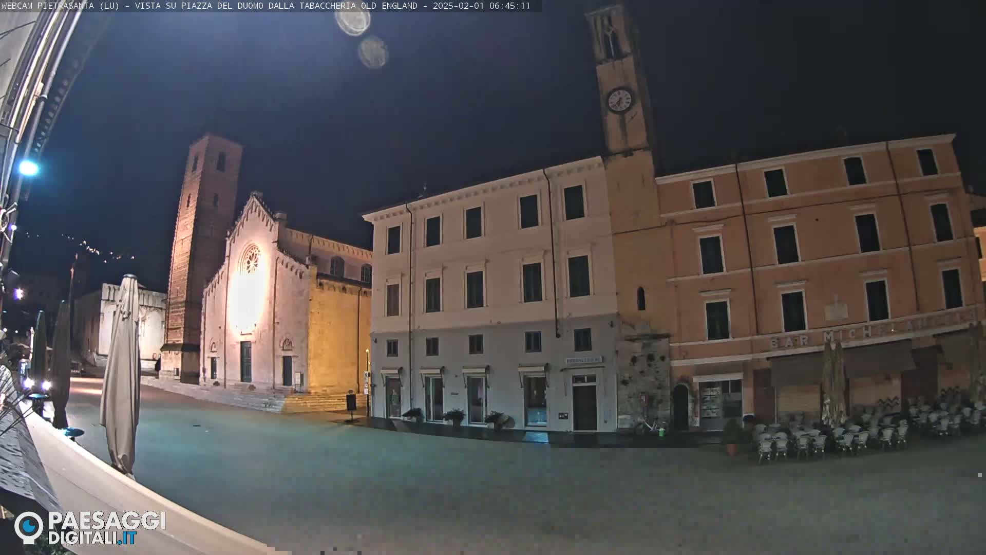A nighttime view of a town square with a church, buildings, and outdoor seating.