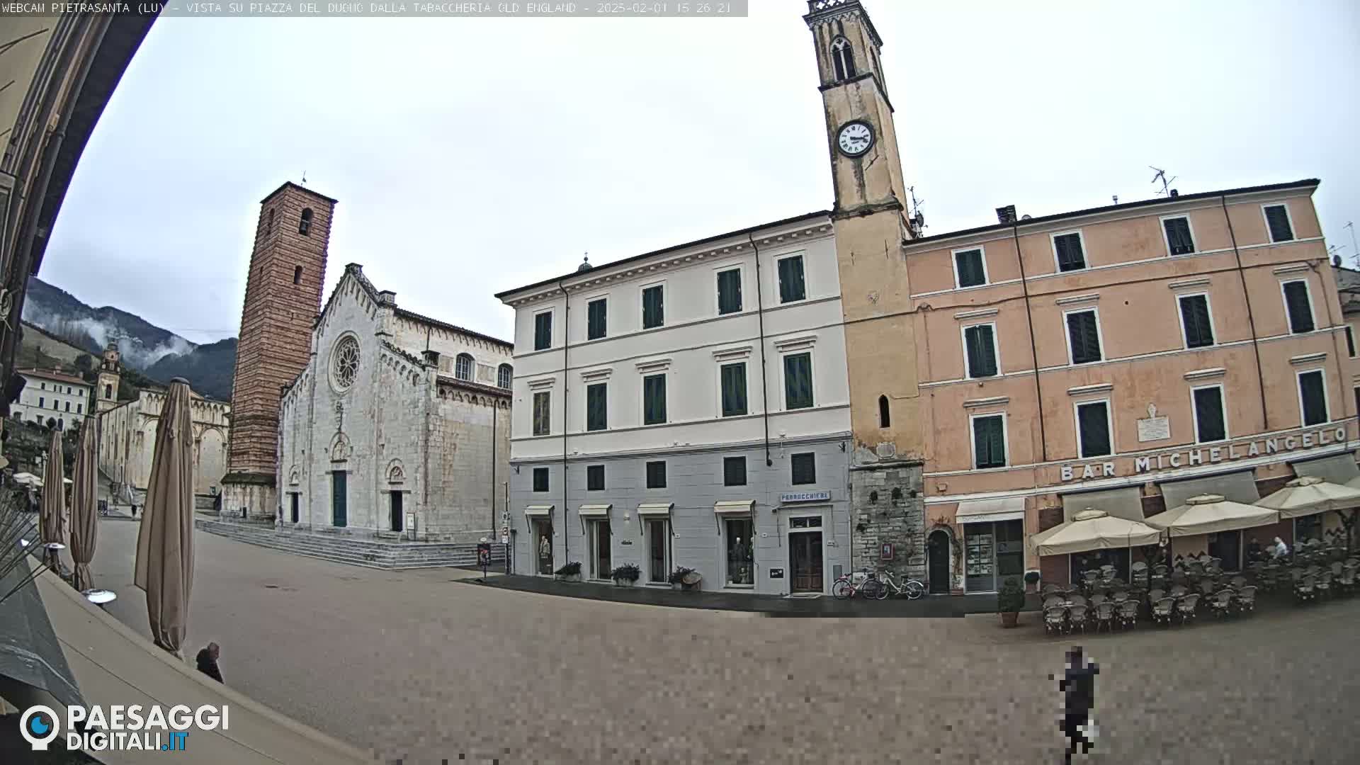 A mostly empty town square on an overcast day, featuring a large stone church, several buildings, and an outdoor cafe with umbrellas.