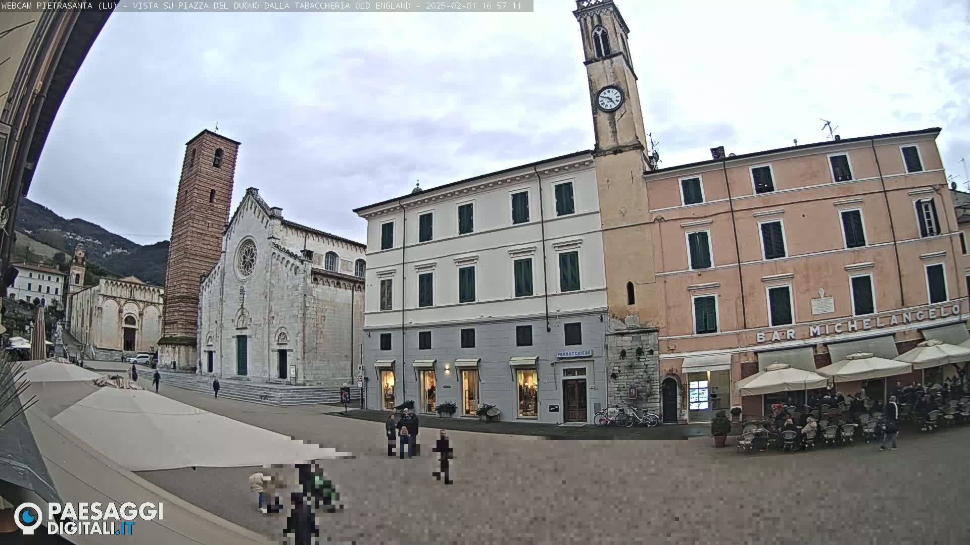 A town square with several buildings, including a church with a tall bell tower, under an overcast sky.