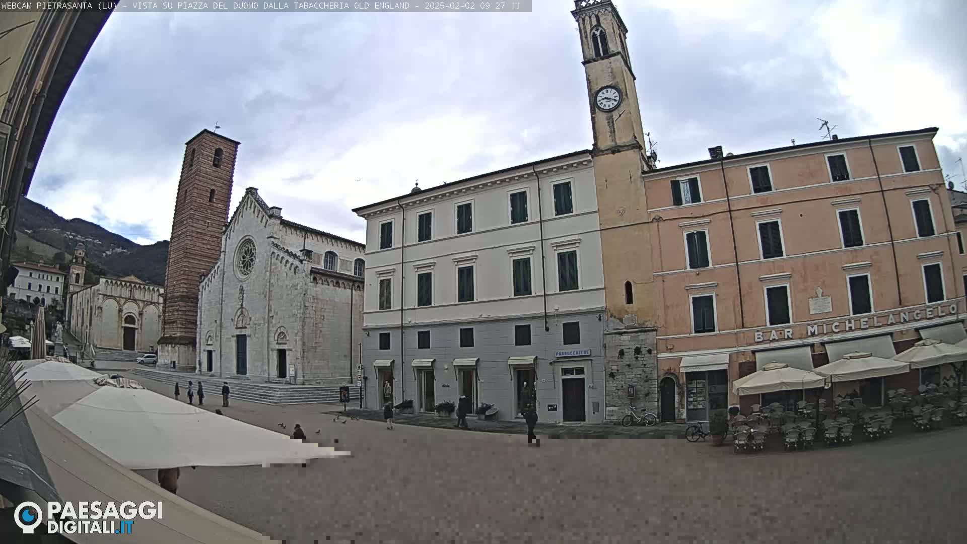 A town square with a large church and several buildings, including a clock tower and a bar, under an overcast sky.