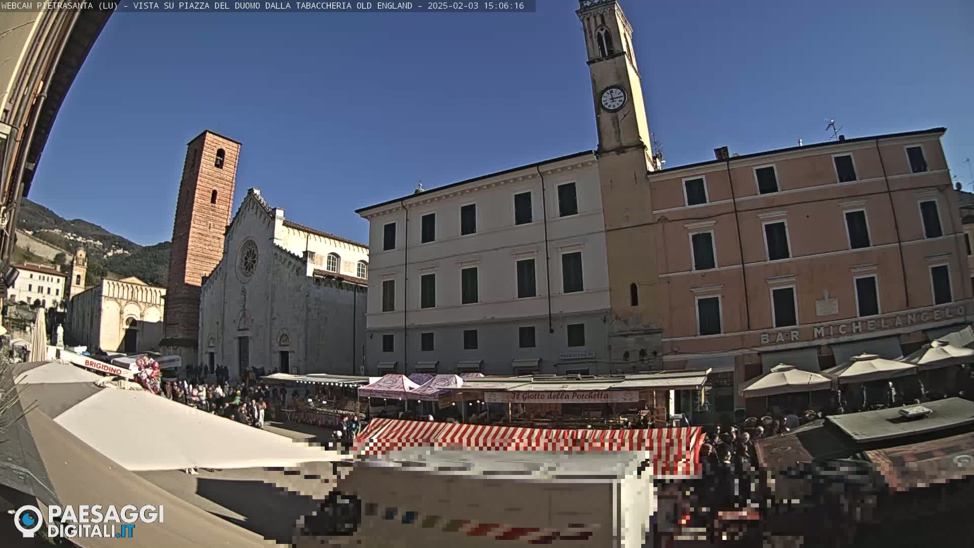 A sunny town square with a cathedral, market stalls, and several buildings, including a clock tower.