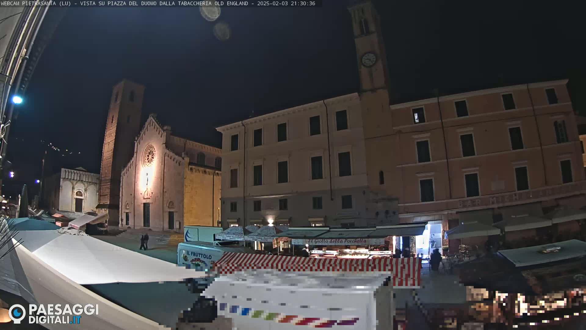 A nighttime view of a town square with a church, buildings, and market stalls under a clear, dark sky.