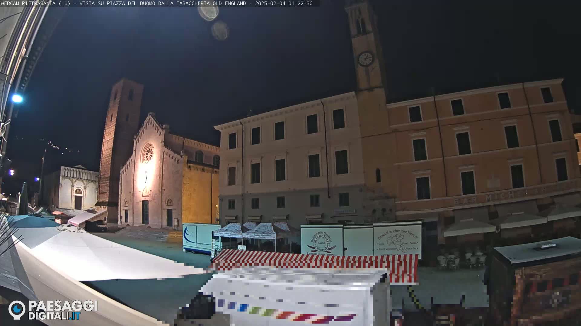 A nighttime view of a town square with a church, buildings, and market stalls under a clear, dark sky.