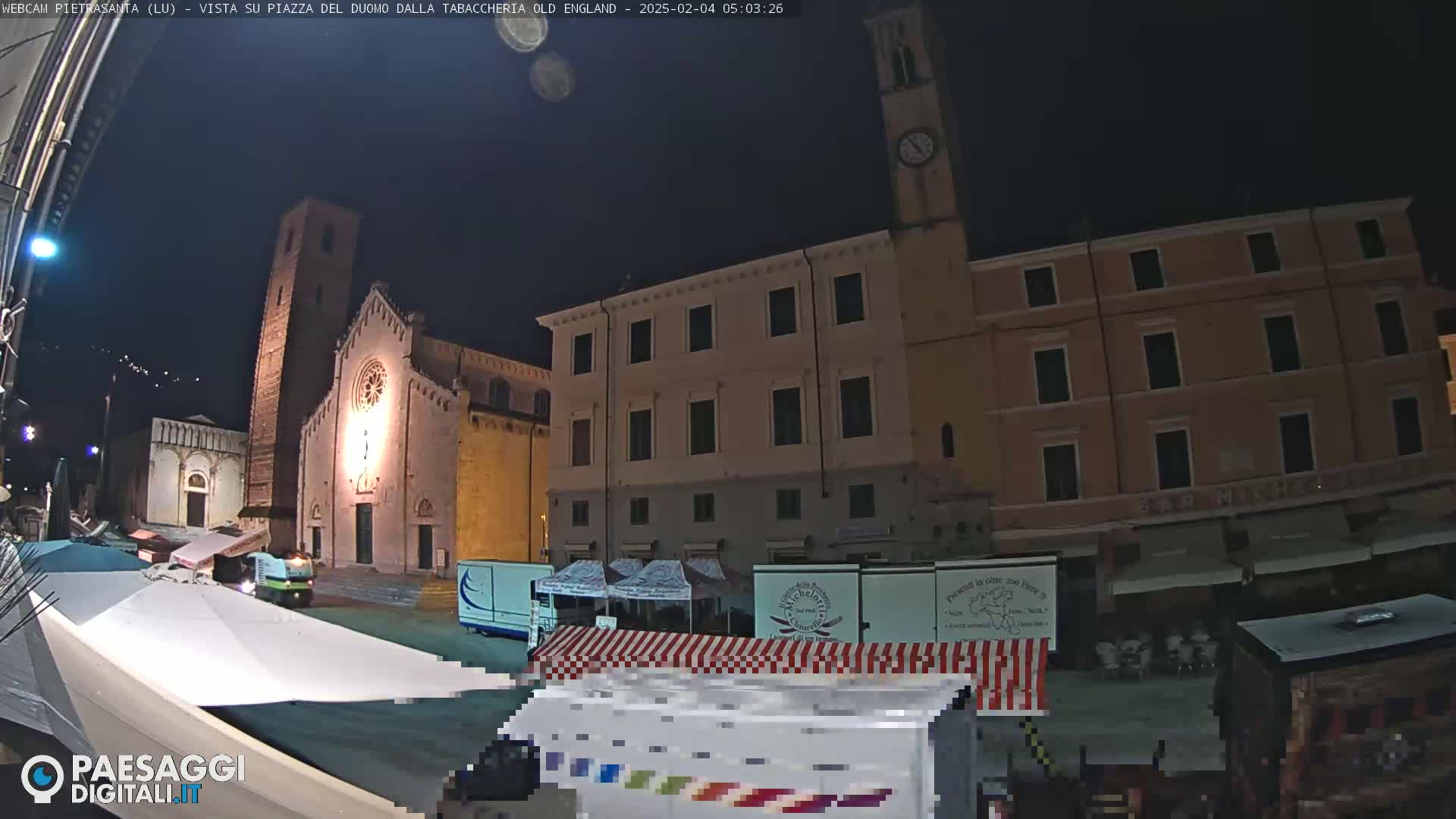 A nighttime view of a town square with a church, buildings, and market stalls under a clear, dark sky.