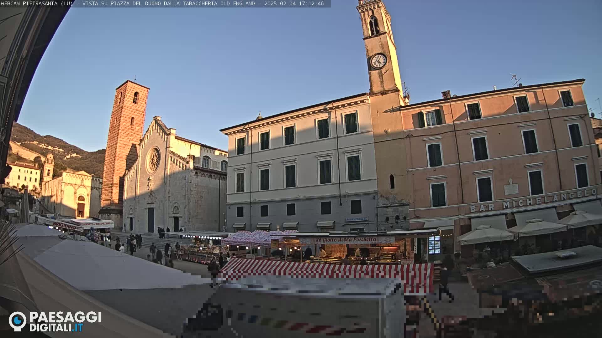 A town square with a market, a church, and buildings under a clear, sunny sky.