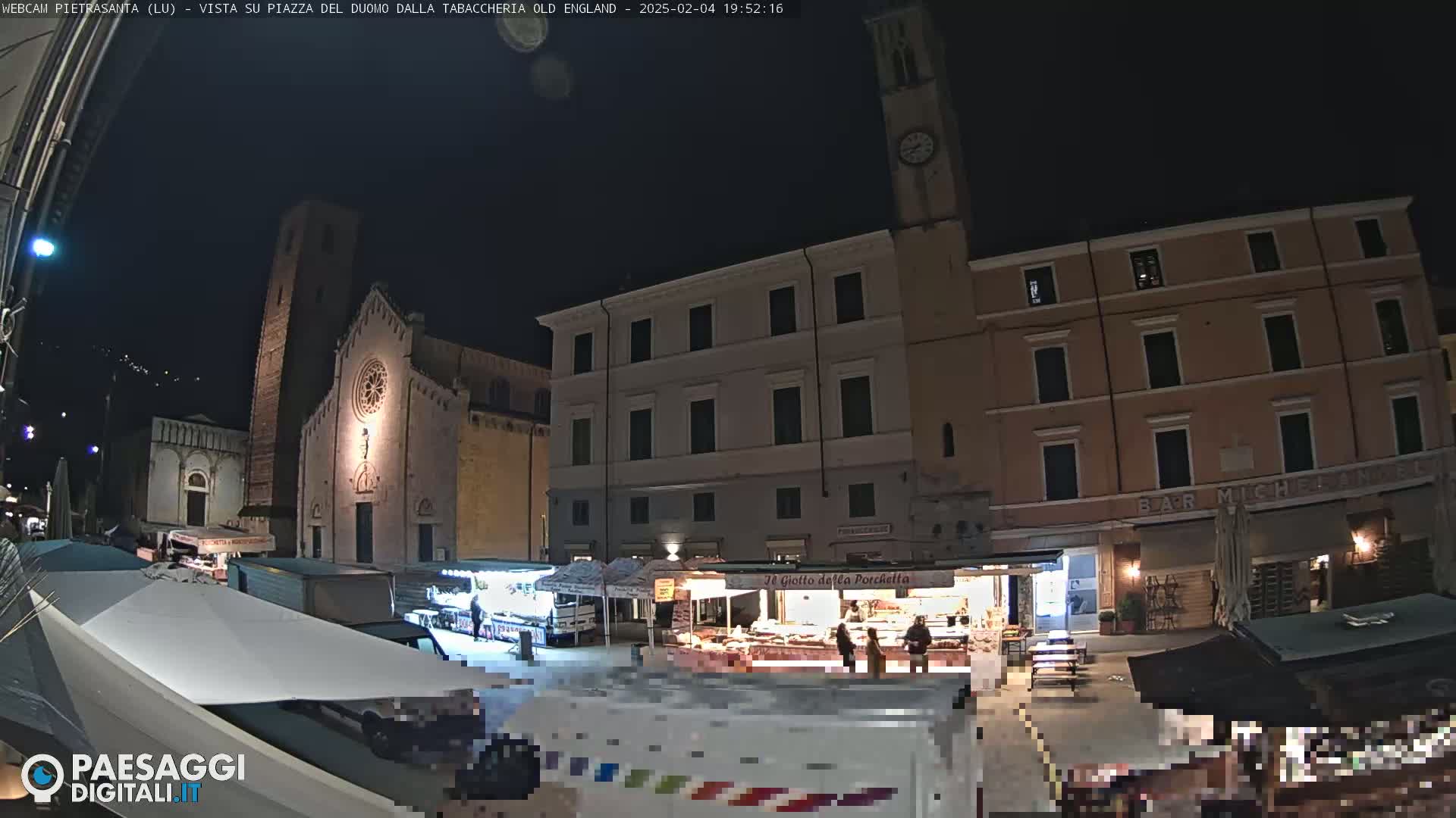 A nighttime view of a town square with a church and market stalls under a clear, dark sky.
