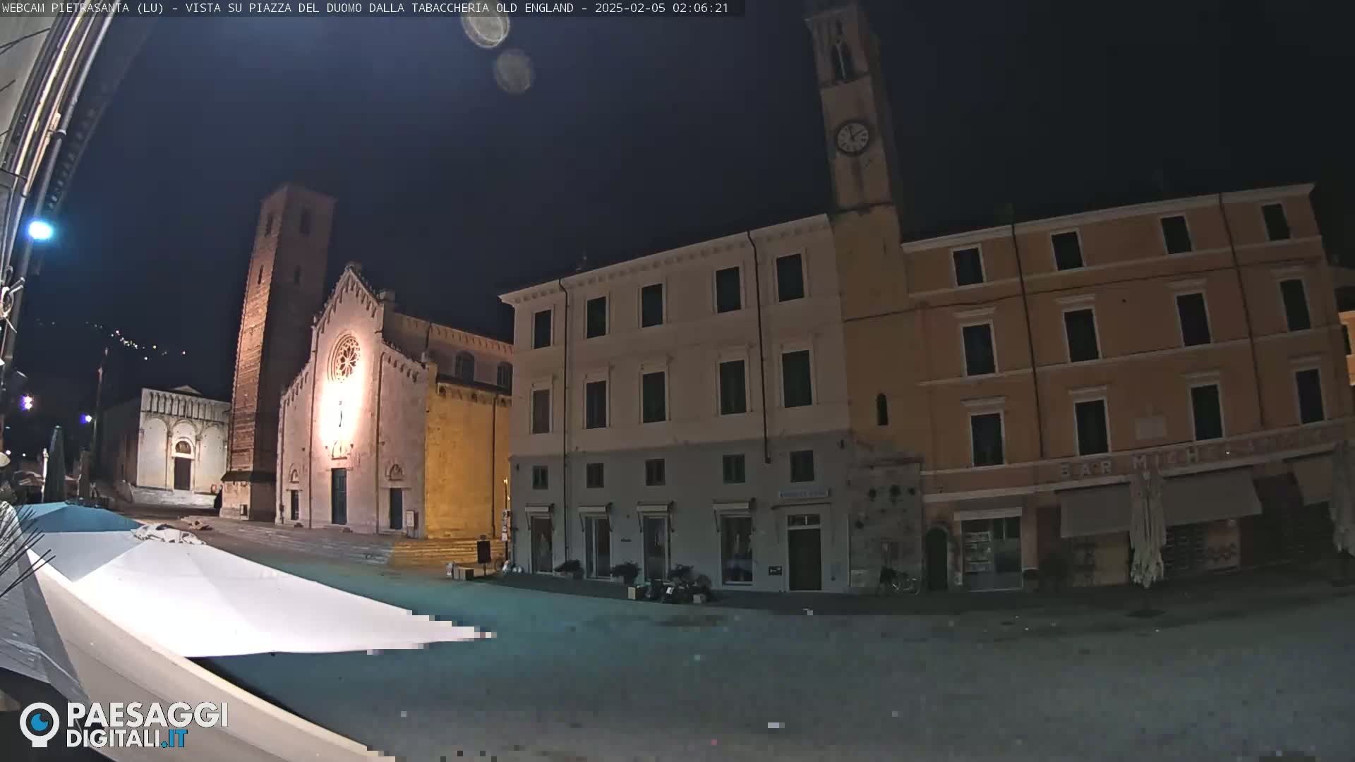 A nighttime view of a town square with buildings illuminated, including a church with a tall bell tower.