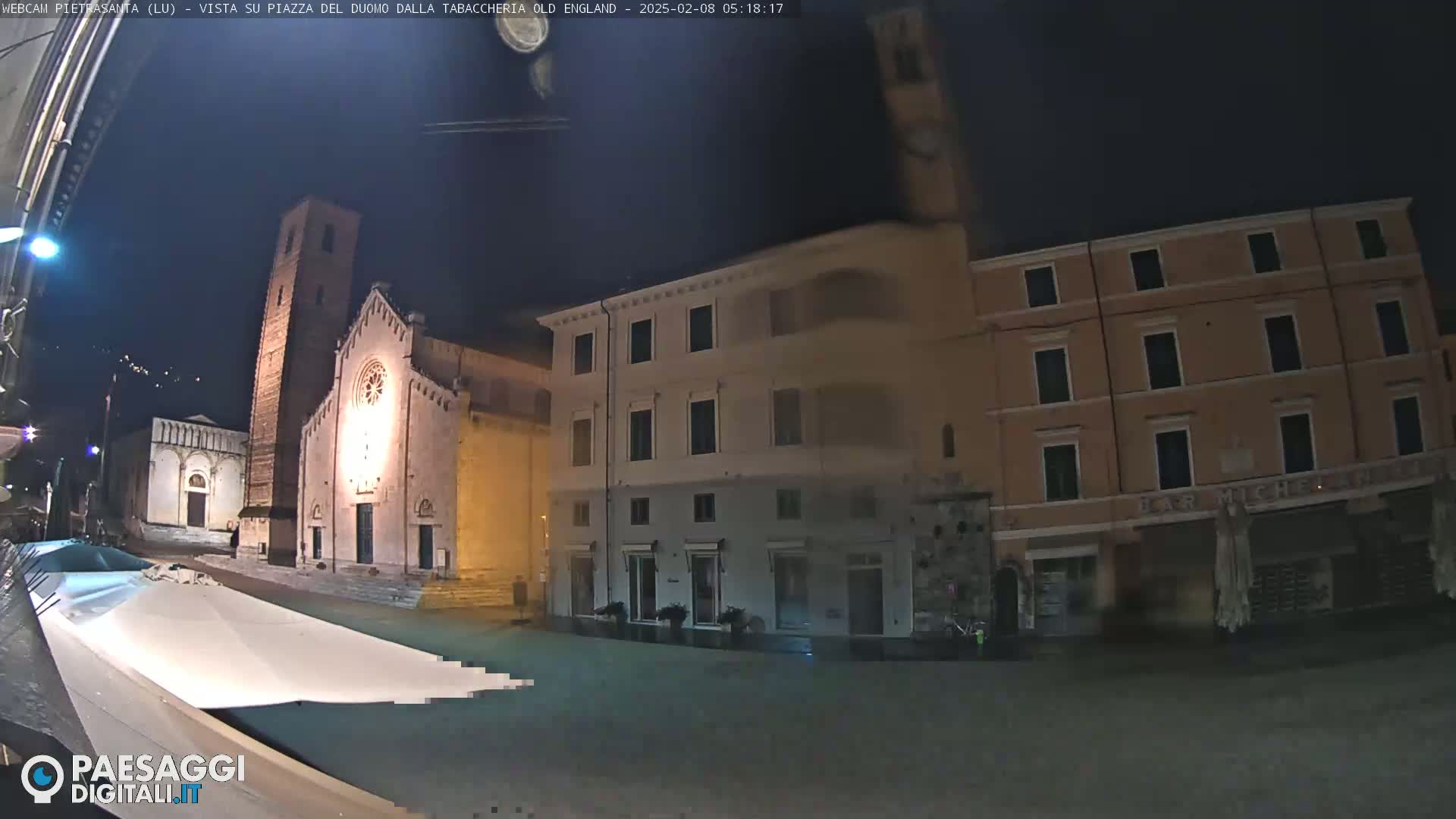 A nighttime view of a town square, featuring a church and several buildings under a dark sky.