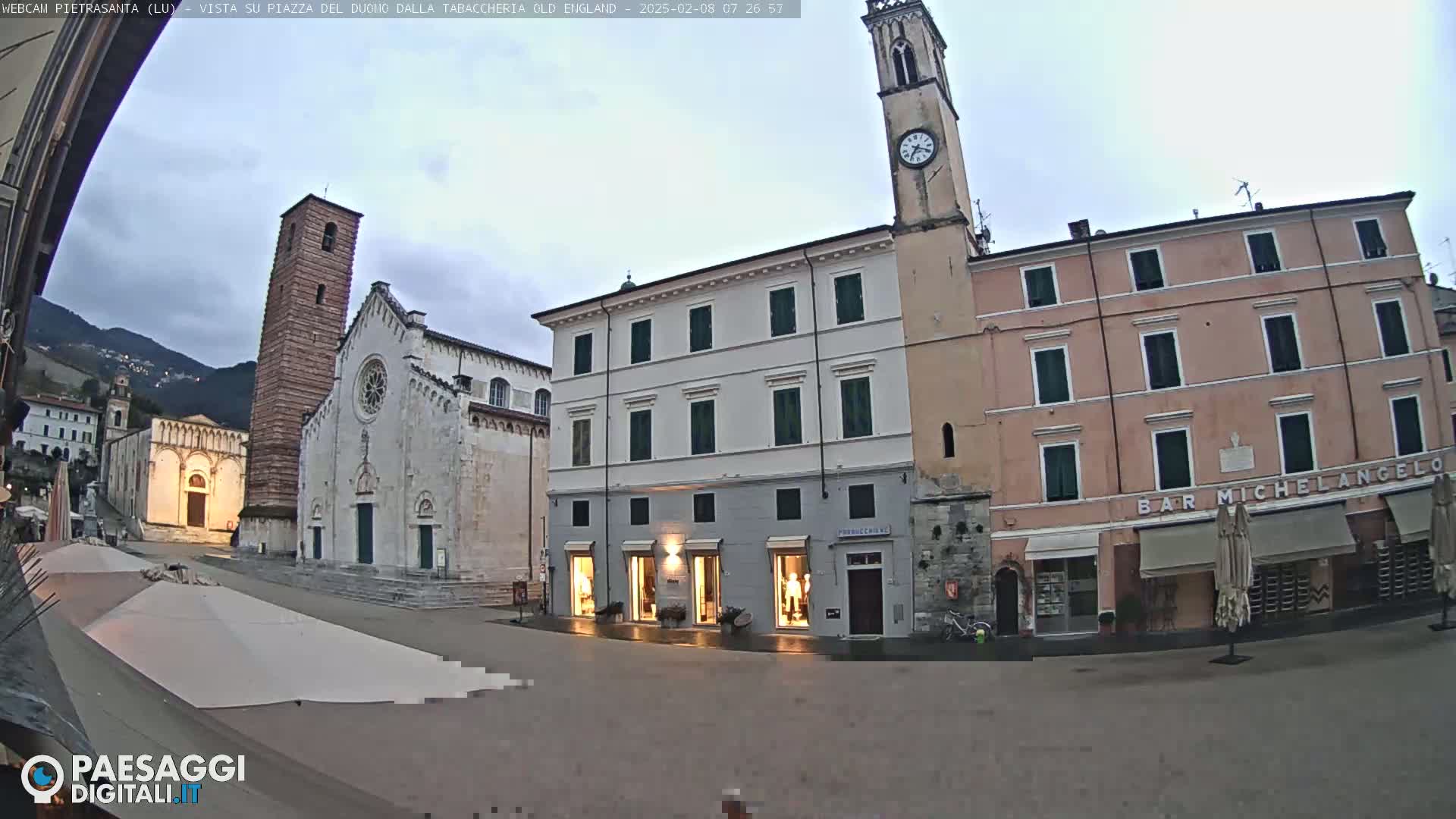 A town square with several buildings, including a church with a tall bell tower, under an overcast sky.