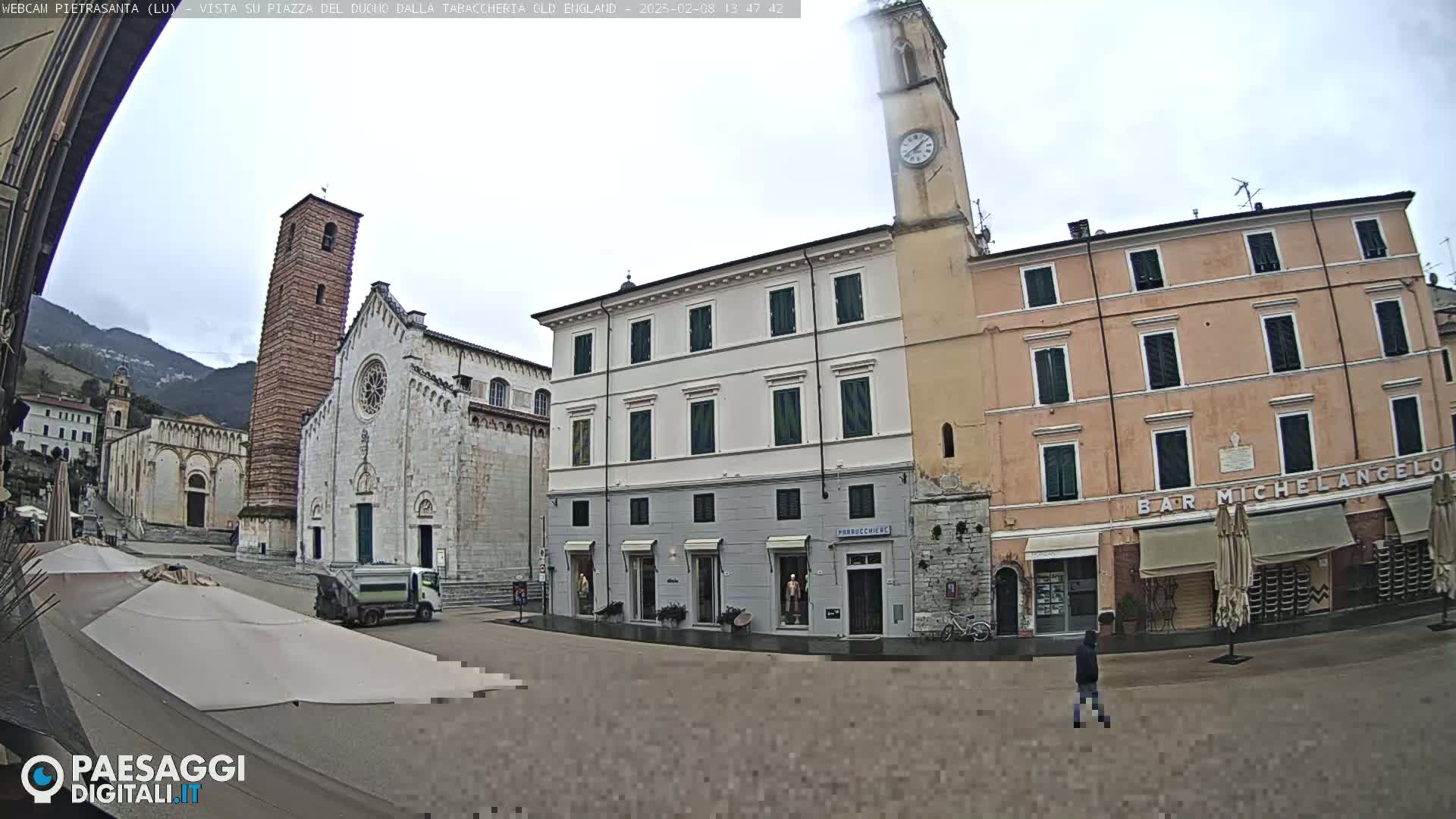 A town square with several buildings, including a church and a clock tower, on an overcast day with wet pavement.