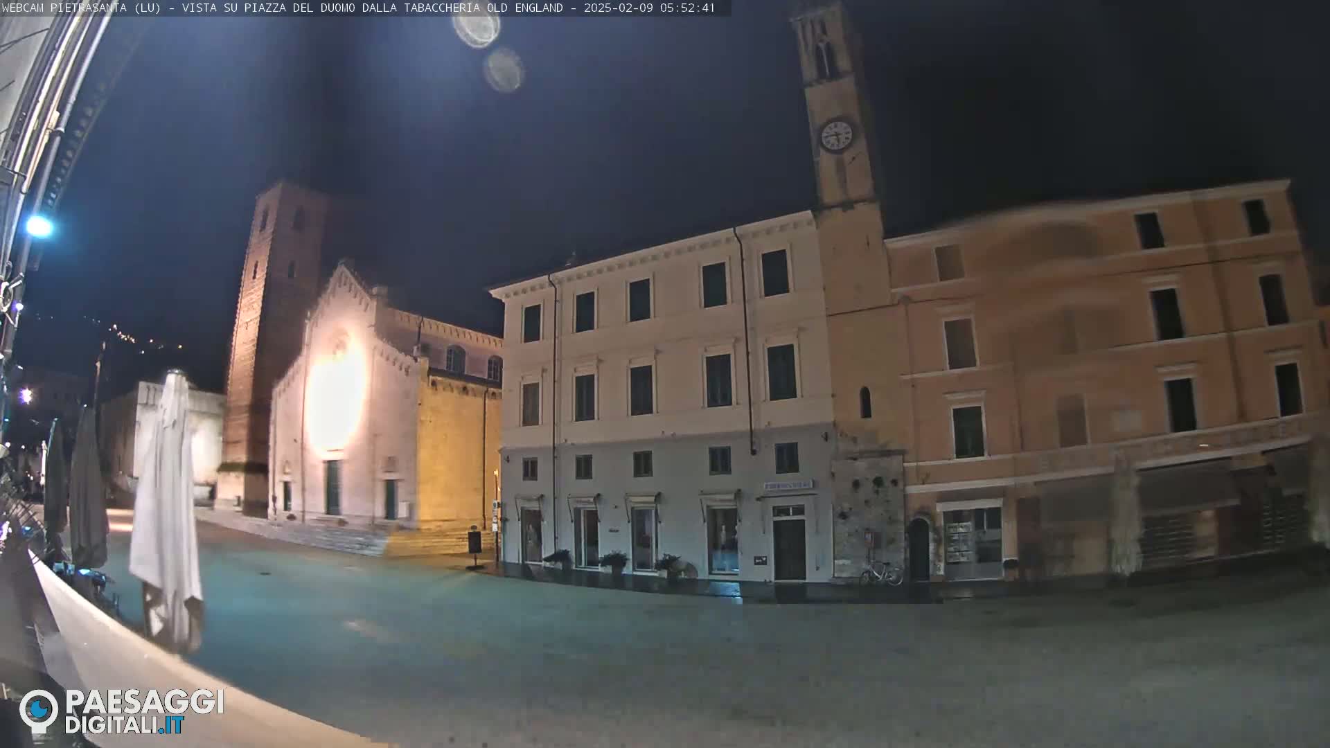 A nighttime view of a town square with several buildings, including a church and a clock tower, under a dark sky.