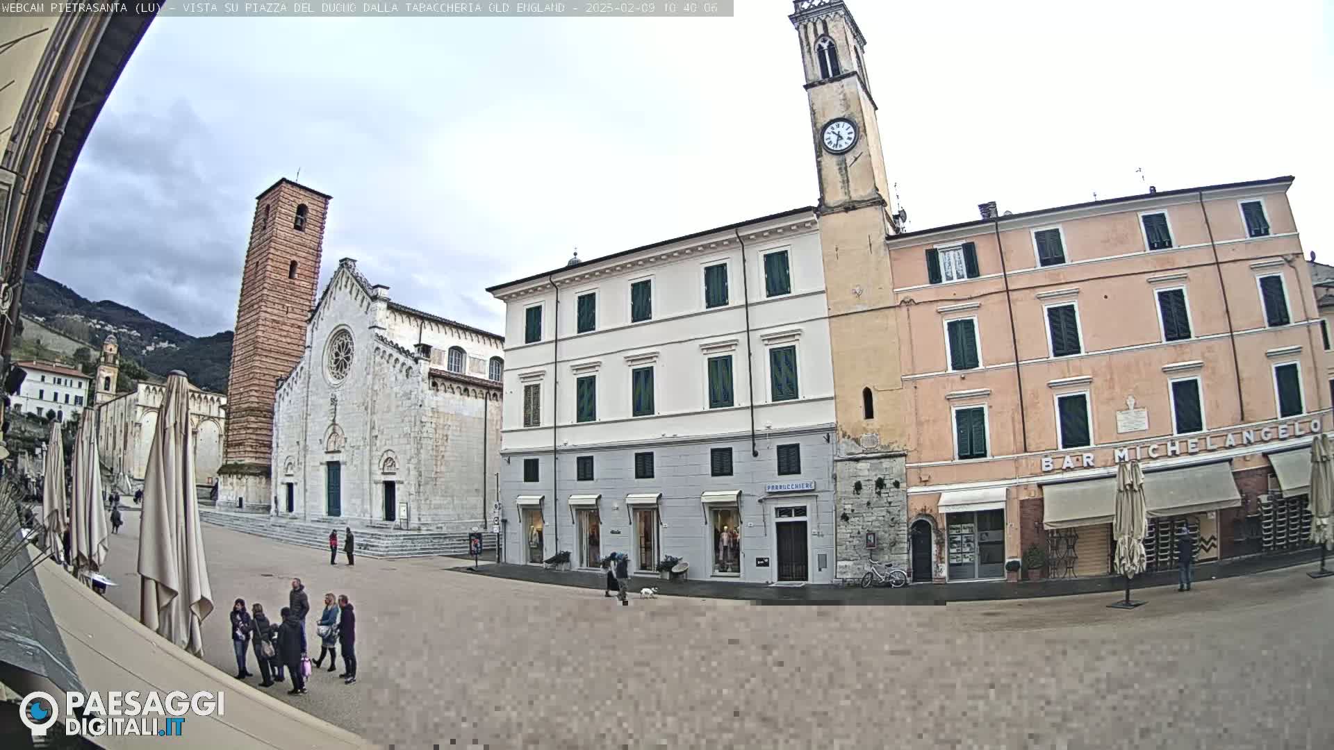 A town square with several buildings, including a church with a tall bell tower, under an overcast sky.
