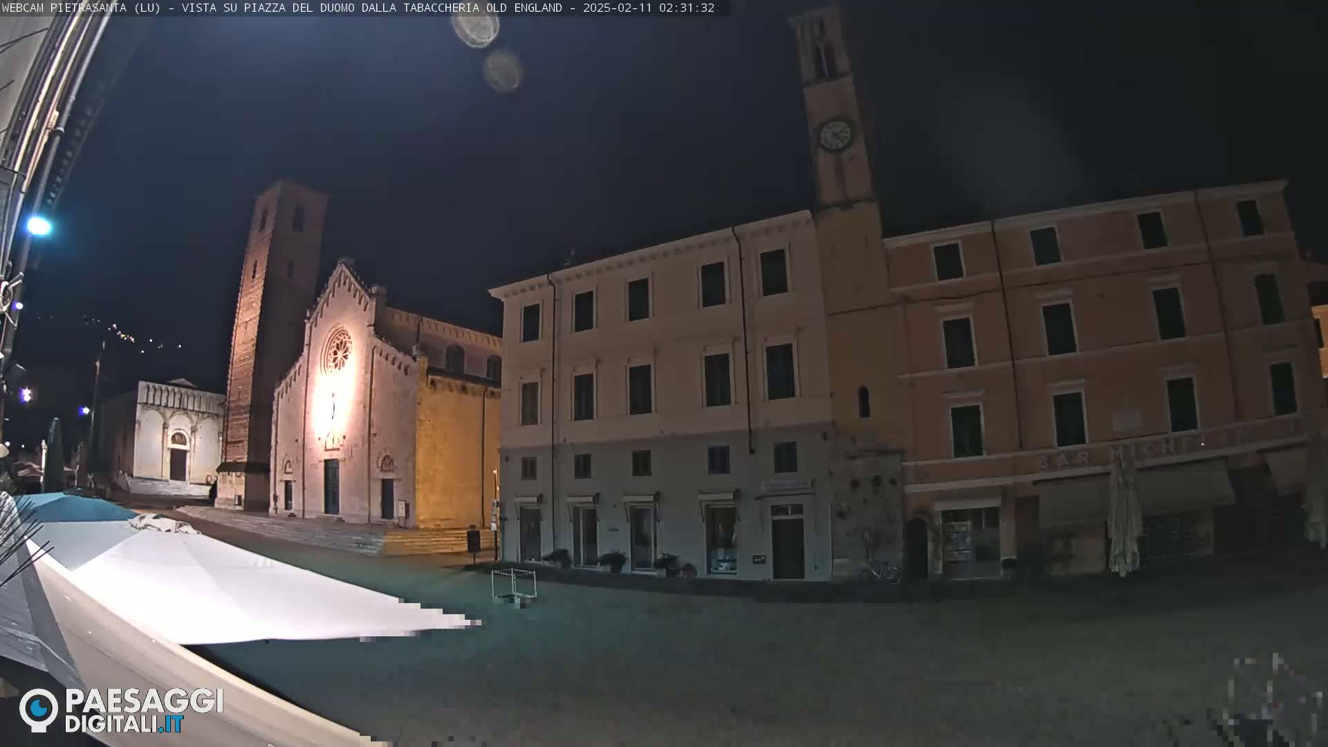 A nighttime view of a town square with a church and several buildings, under a dark sky.