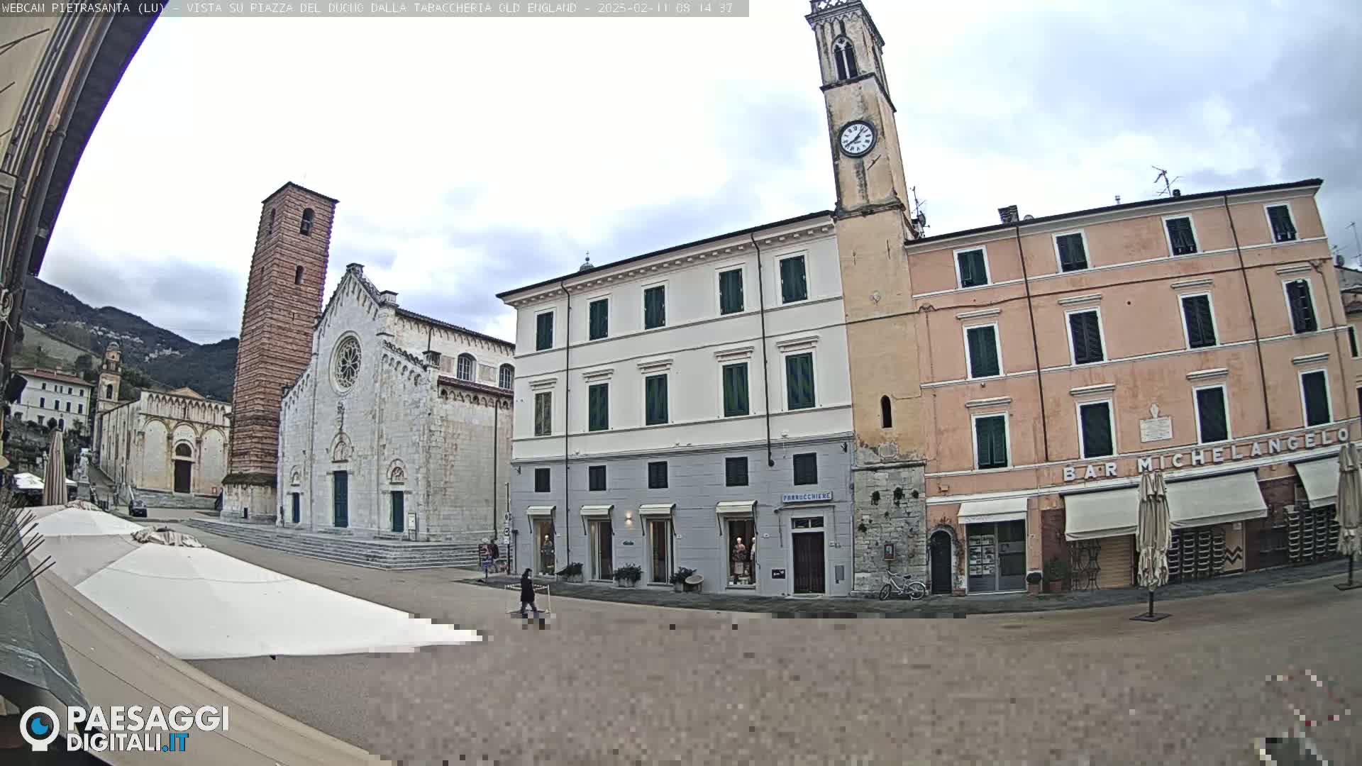 A town square with a large cathedral, multi-story buildings, and a clock tower under an overcast sky.