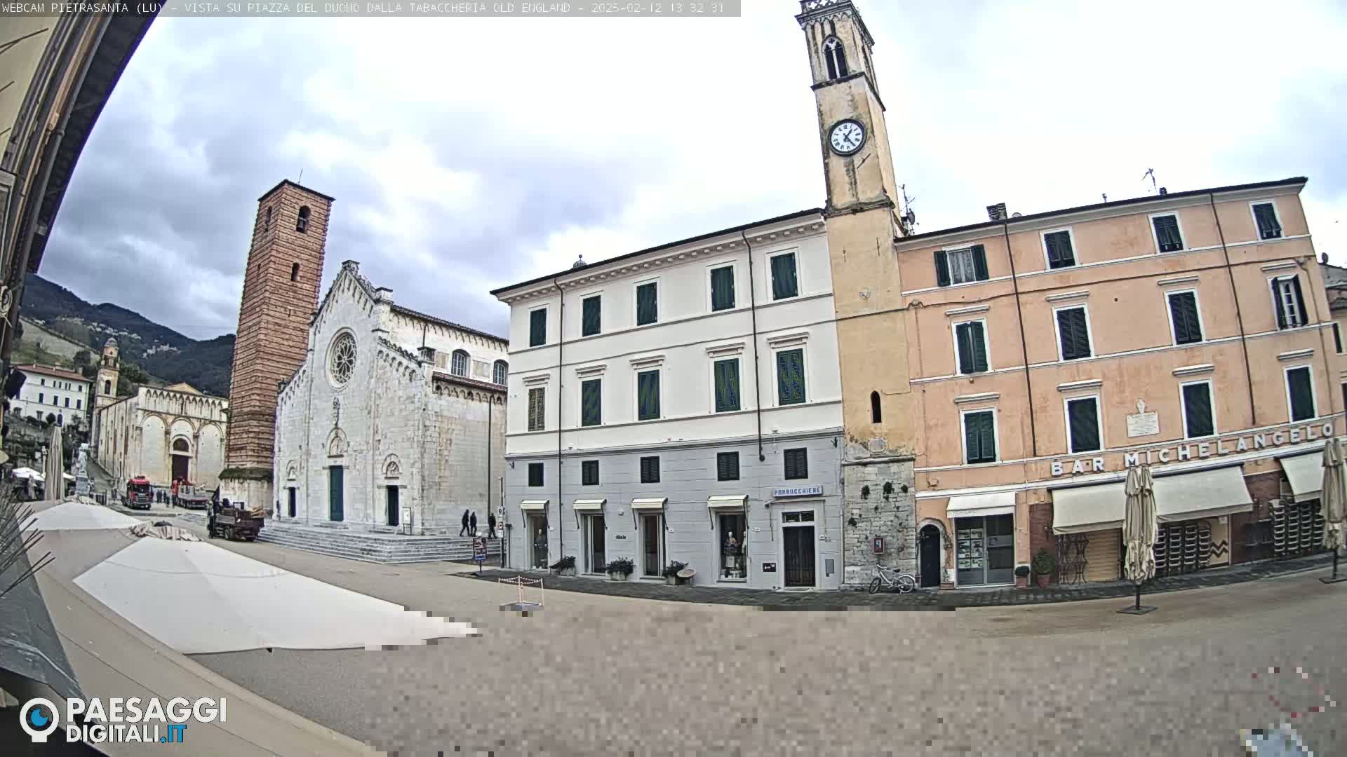 A town square with a large stone church, a clock tower, and several buildings, under an overcast sky.