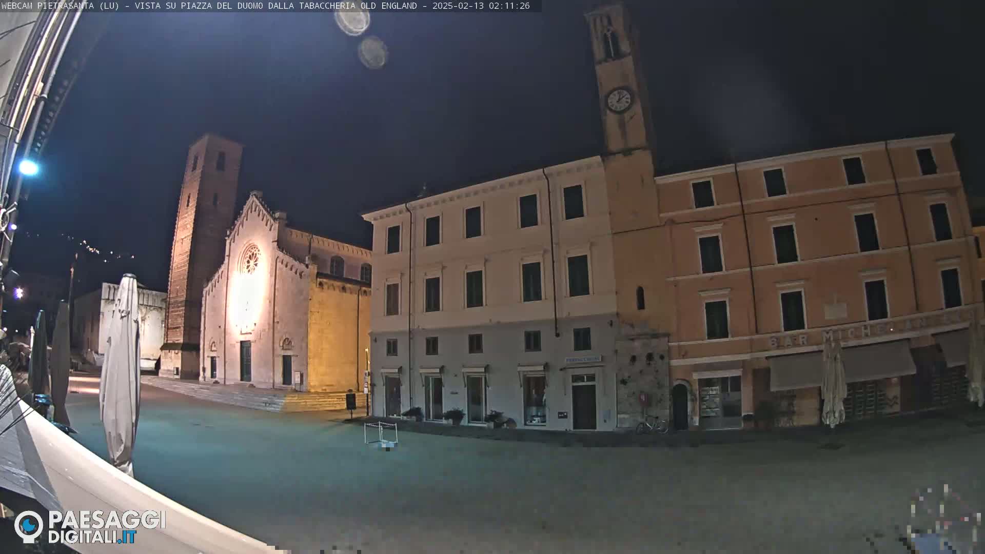 A nighttime view of a town square with a church and buildings, under a dark, clear sky.