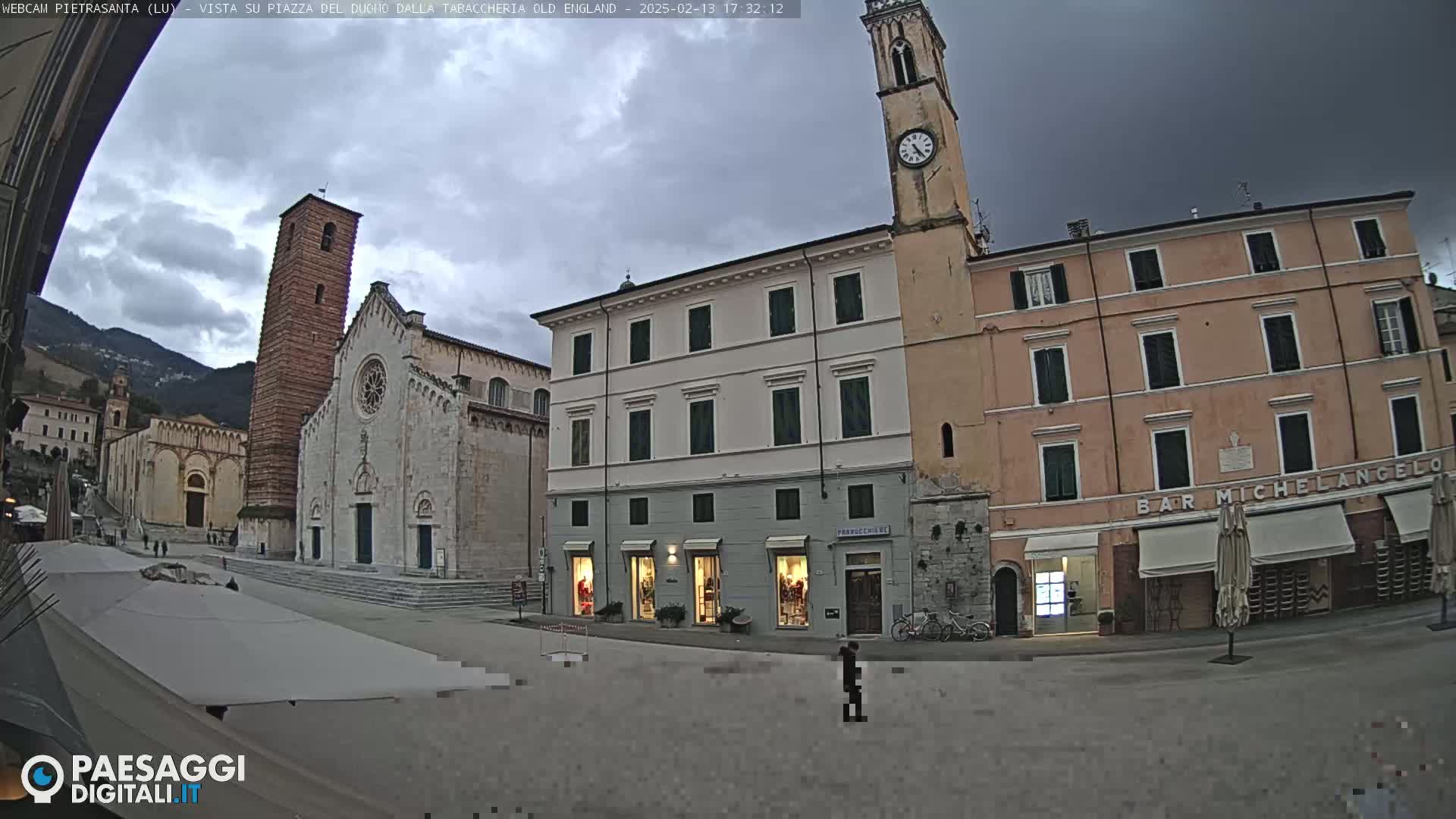 A town square with a large stone church and clock tower under an overcast sky.