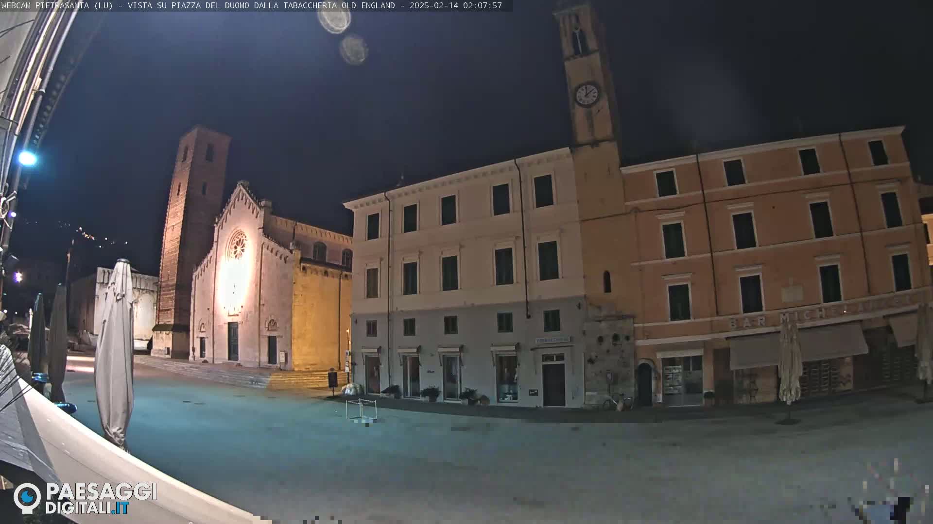 A nighttime view of a town square with a church and buildings under a clear, dark sky.