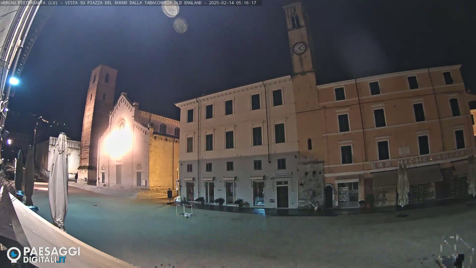 A nighttime view of a town square with a church and buildings, under a dark sky.