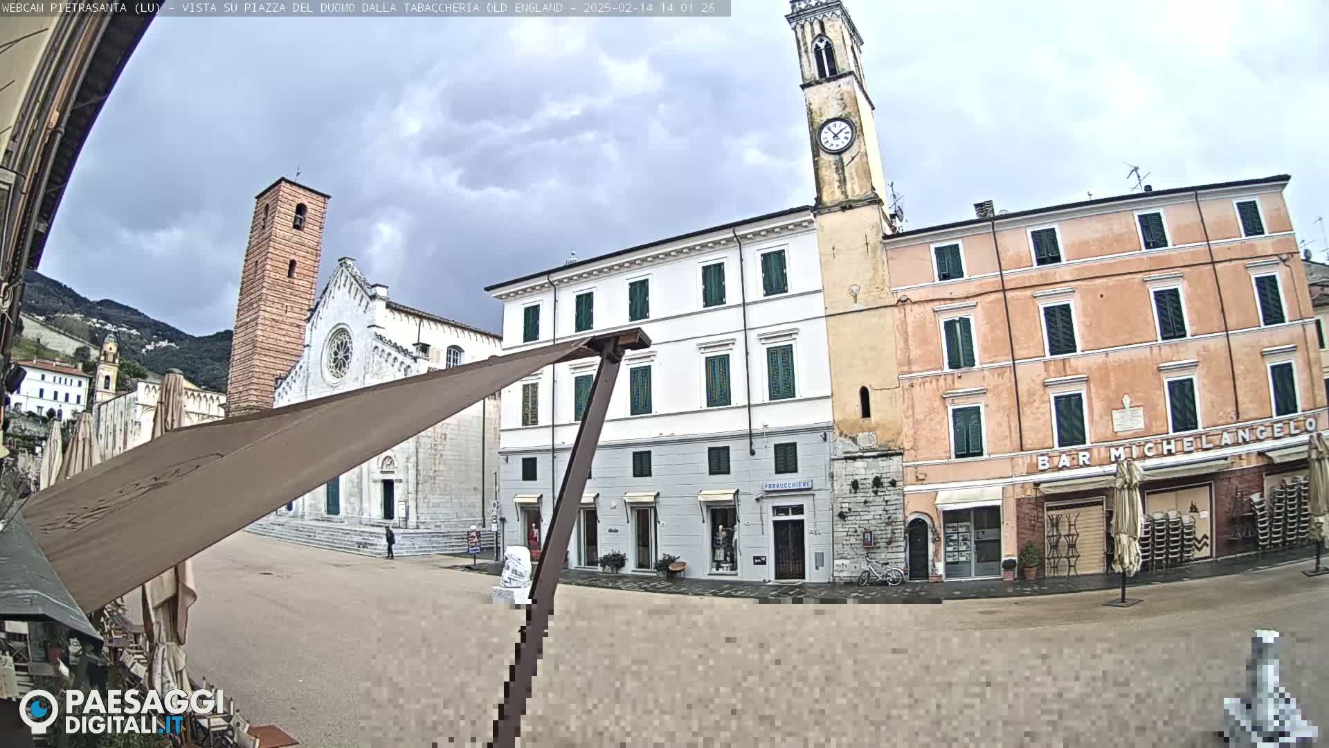 A town square is shown with several buildings, including a church with a tall bell tower, under a cloudy sky.