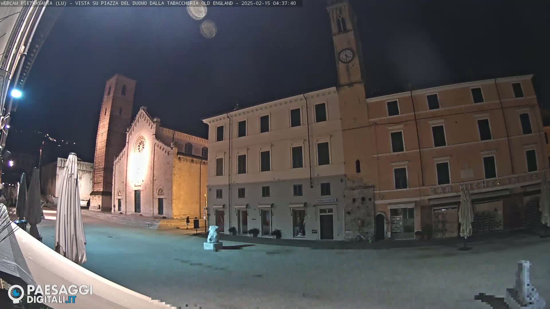 A nighttime view of a town square with a church and buildings, under a dark sky.