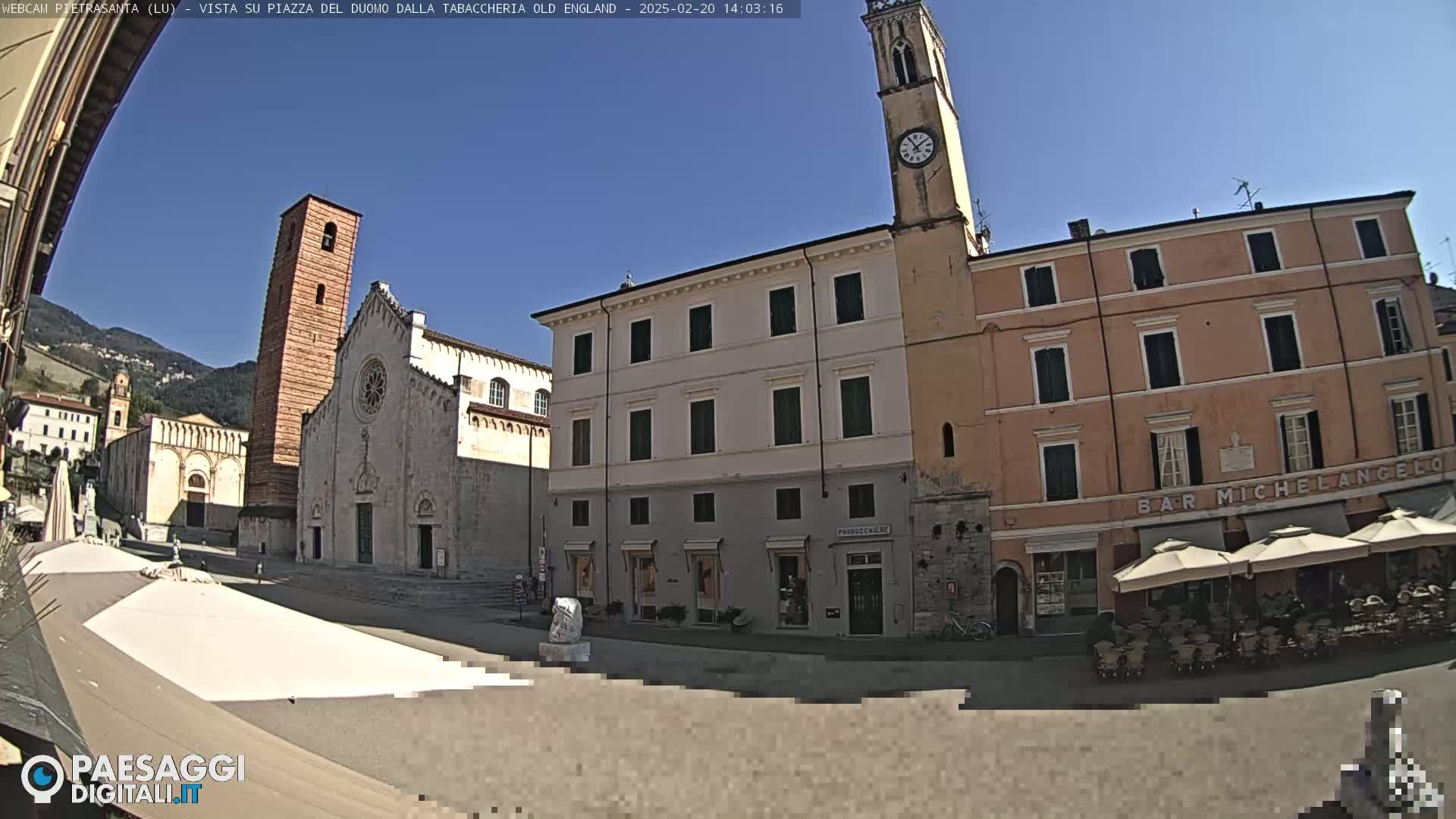 A sunny town square is shown with several buildings, including a church with a tall bell tower, and a cafe with outdoor seating.