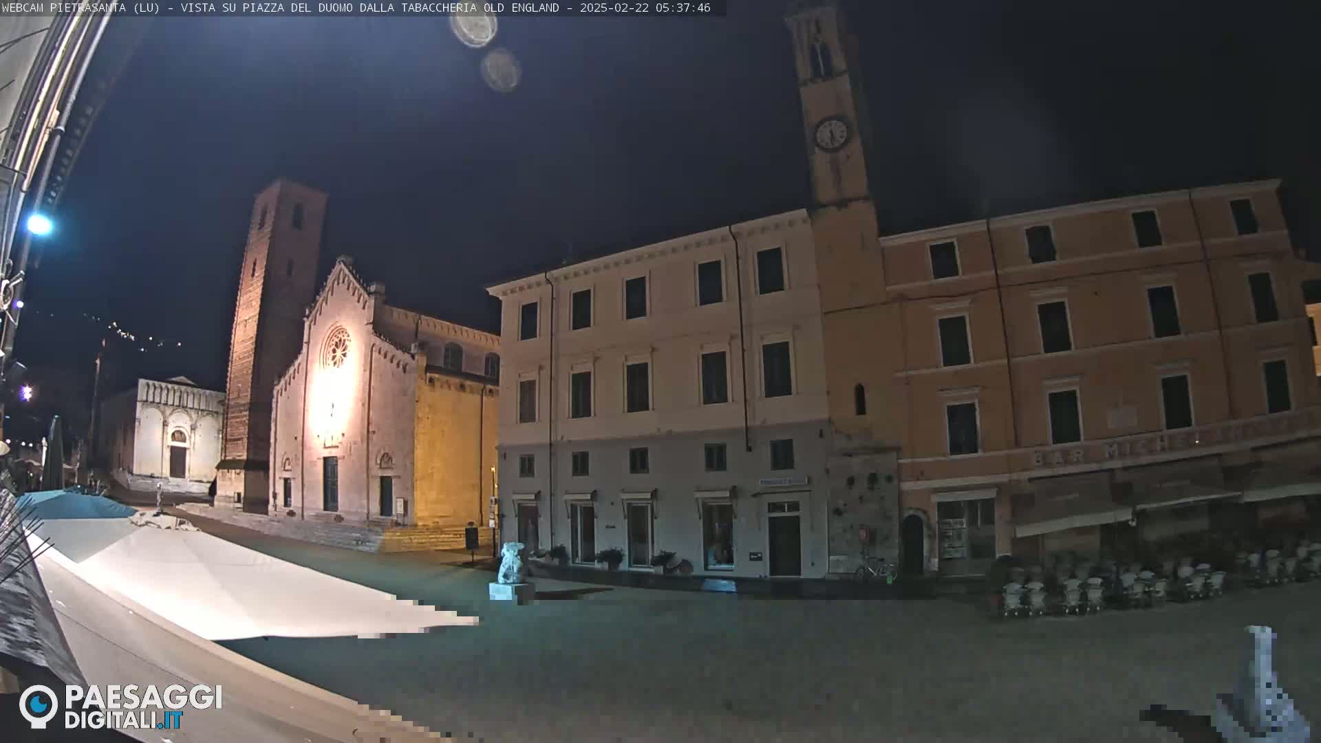 A nighttime view of a town square with a church and buildings, under a dark sky.