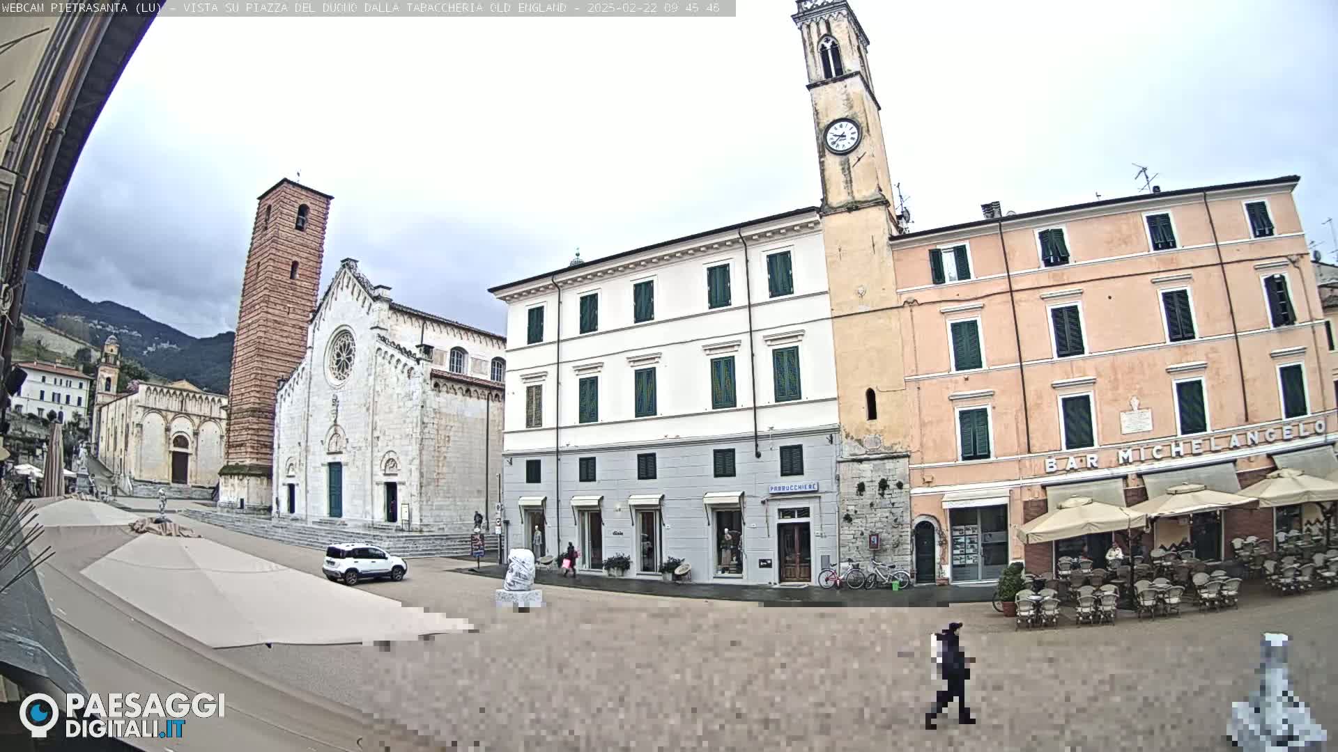 A town square with several buildings, including a church and a clock tower, under an overcast sky.