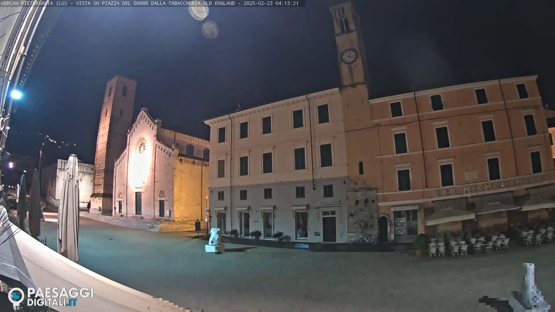 A nighttime view of a town square with a church, several buildings, and outdoor seating.