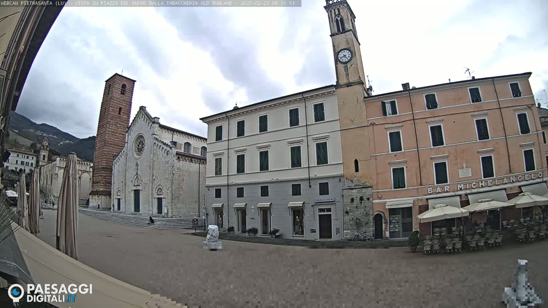 A town square with a church, clock tower, and buildings under an overcast sky.