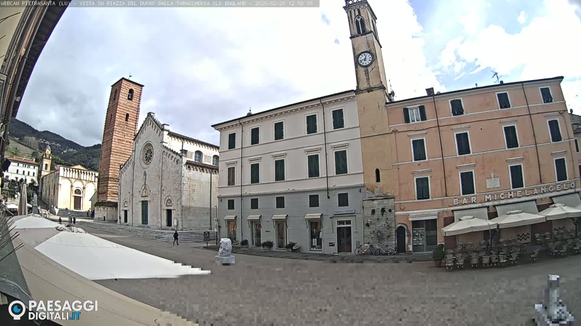 A town square with a large church and several buildings, under a partly cloudy sky.