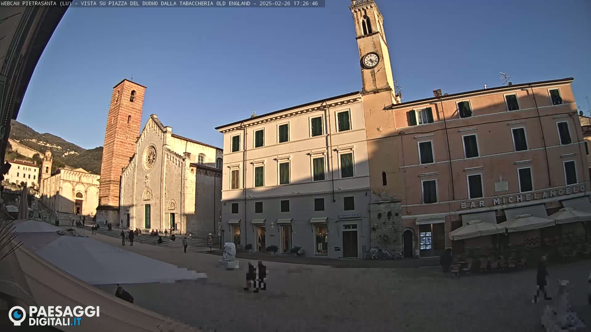 A town square with a church and clock tower, under a clear blue sky.