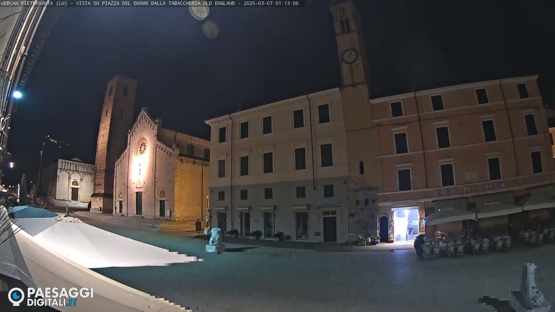 A nighttime view of a town square with a church and several buildings, under a clear, dark sky.
