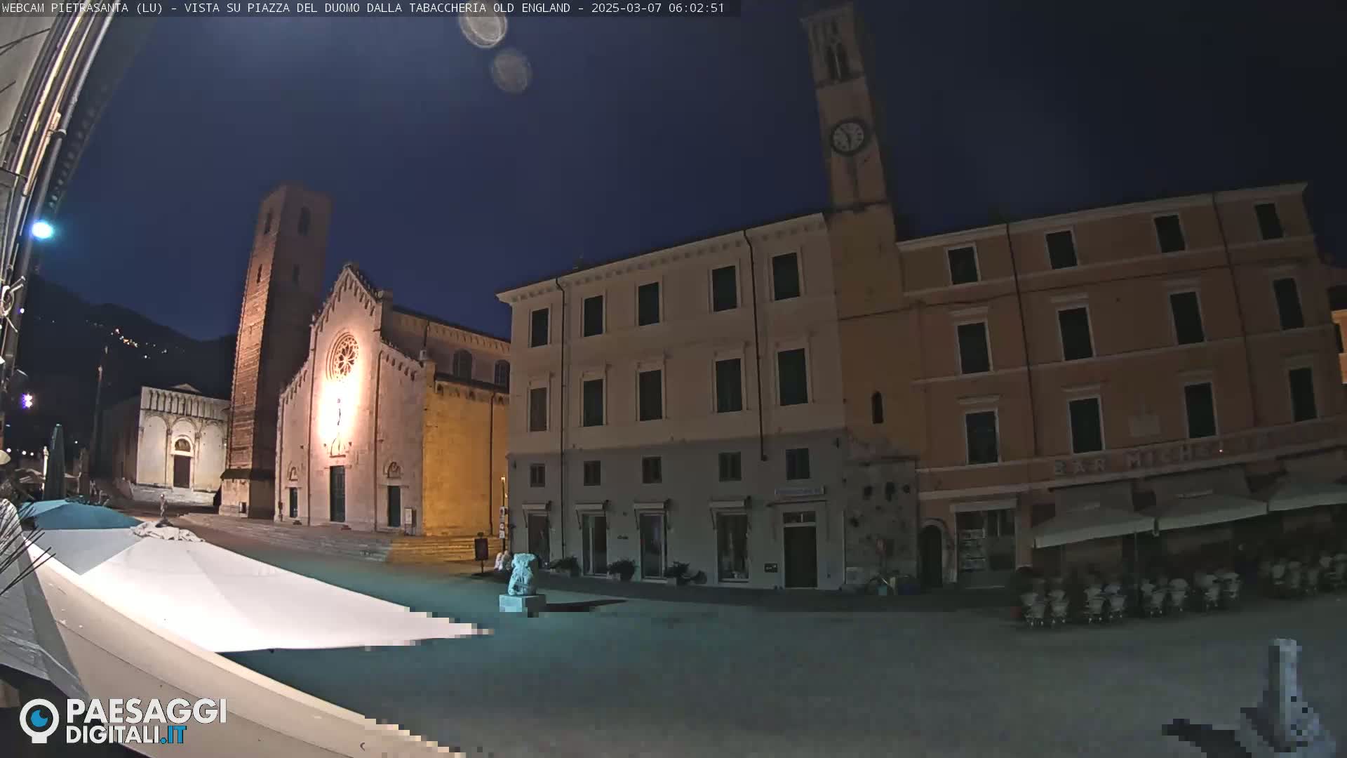 A nighttime view of a town square with a church and buildings under a dark, clear sky.