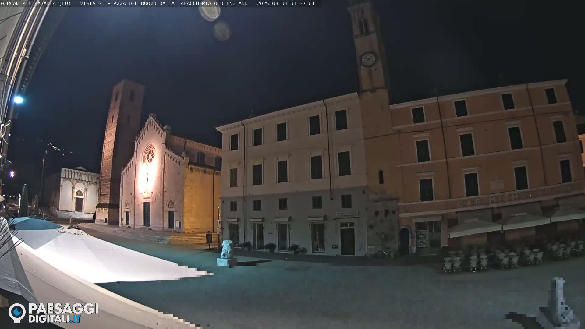 A nighttime view of a town square with a church and buildings, under a clear, dark sky.