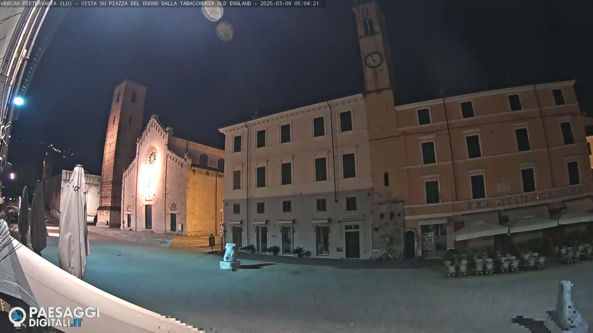 A nighttime view of a town square with a church and buildings, under a dark sky.