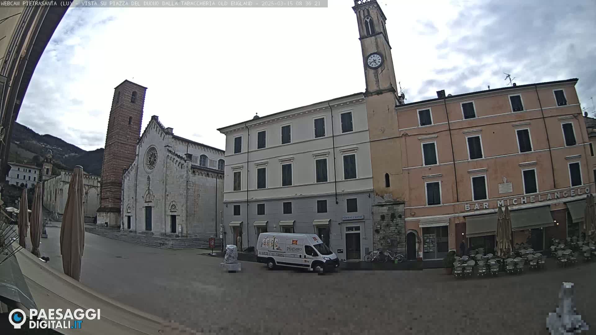 A town square with a church, several buildings, a van, and outdoor seating is visible under an overcast sky.
