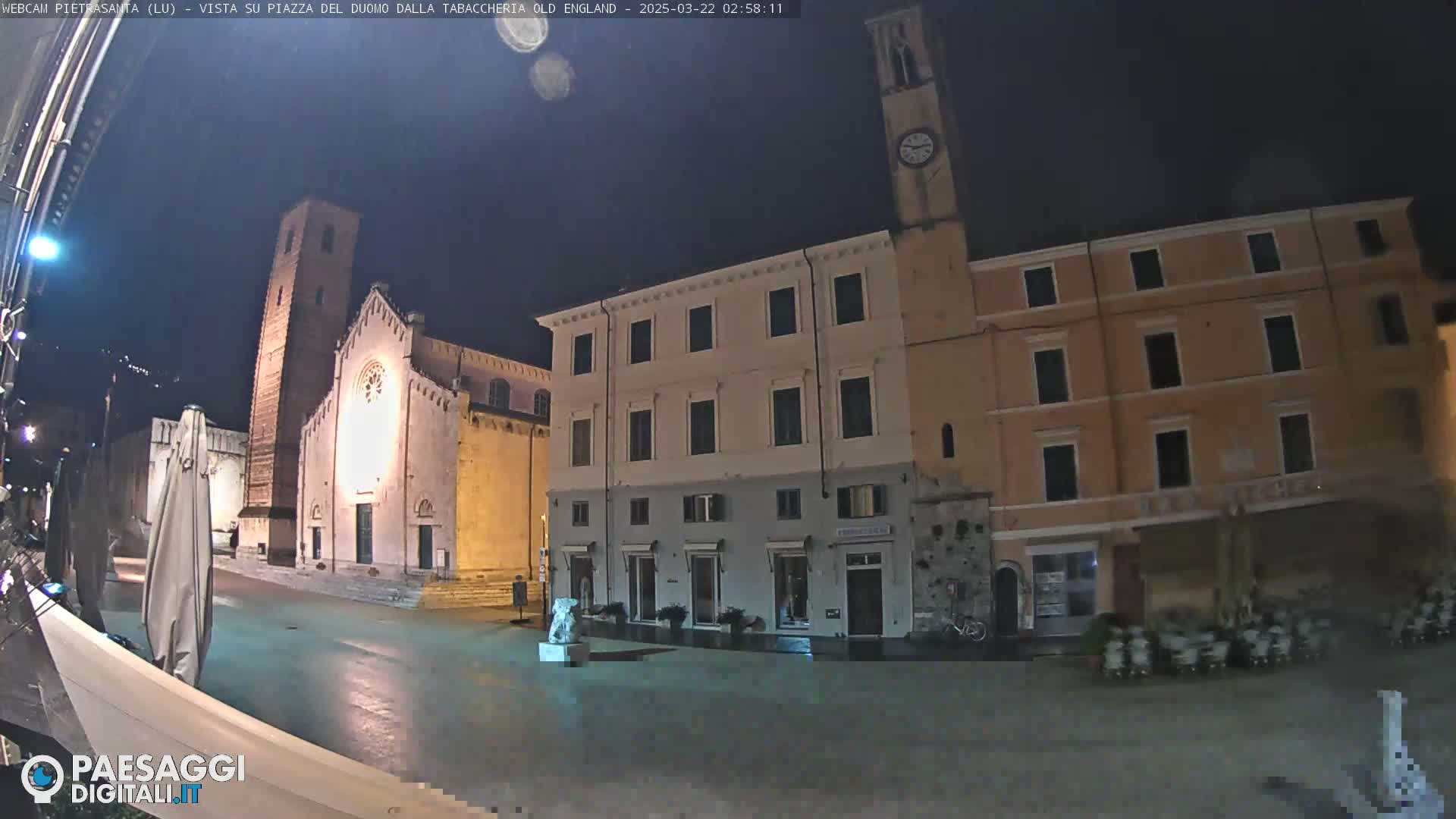 A nighttime view of a town square with a church and buildings, under a dark sky.