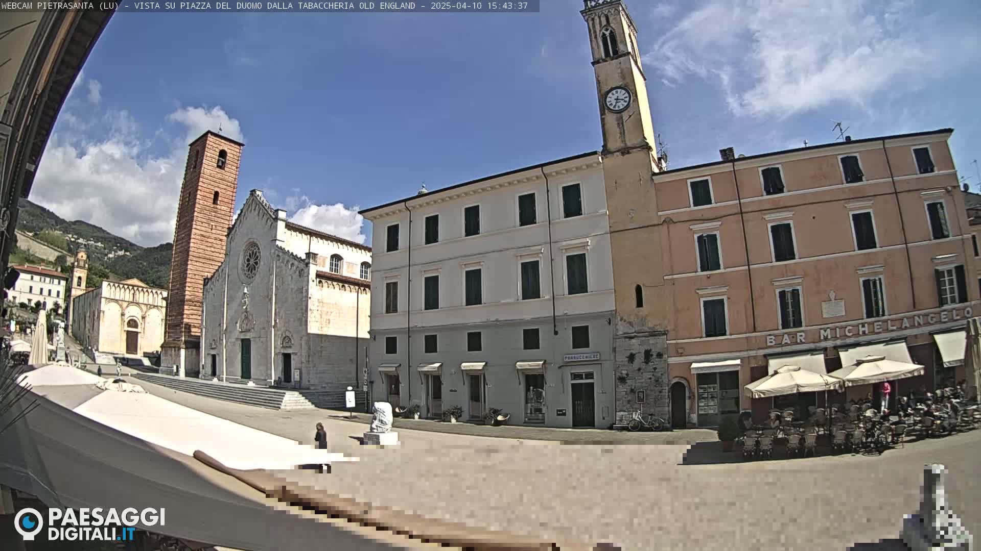 A town square with a church, bell tower, and buildings under a mostly sunny sky.