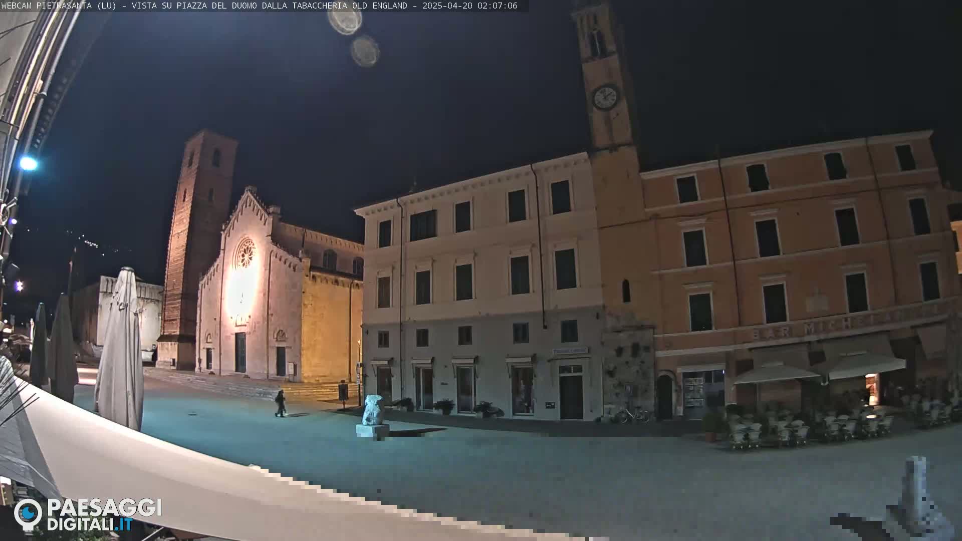 A nighttime view of a town square with a church and buildings, under a clear, dark sky.