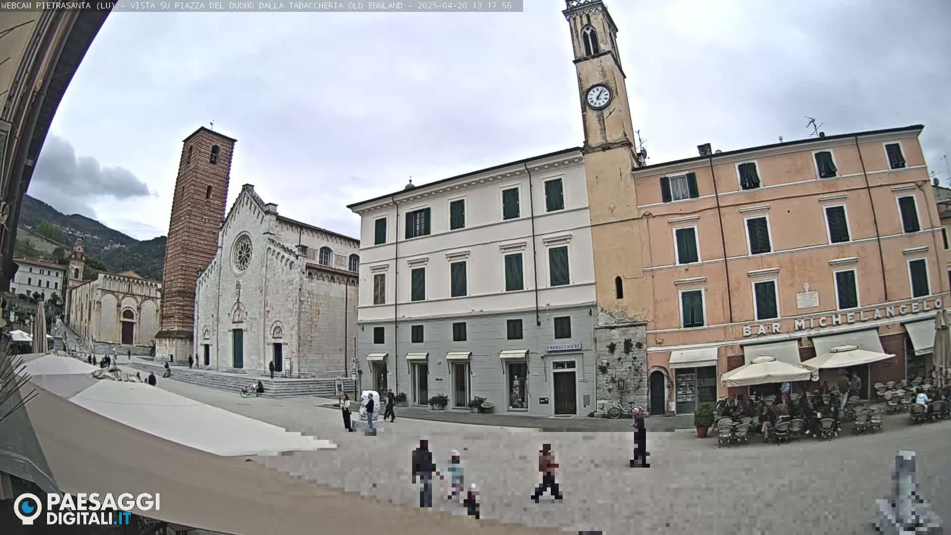 A town square with several buildings, including a large church and clock tower, under an overcast sky.