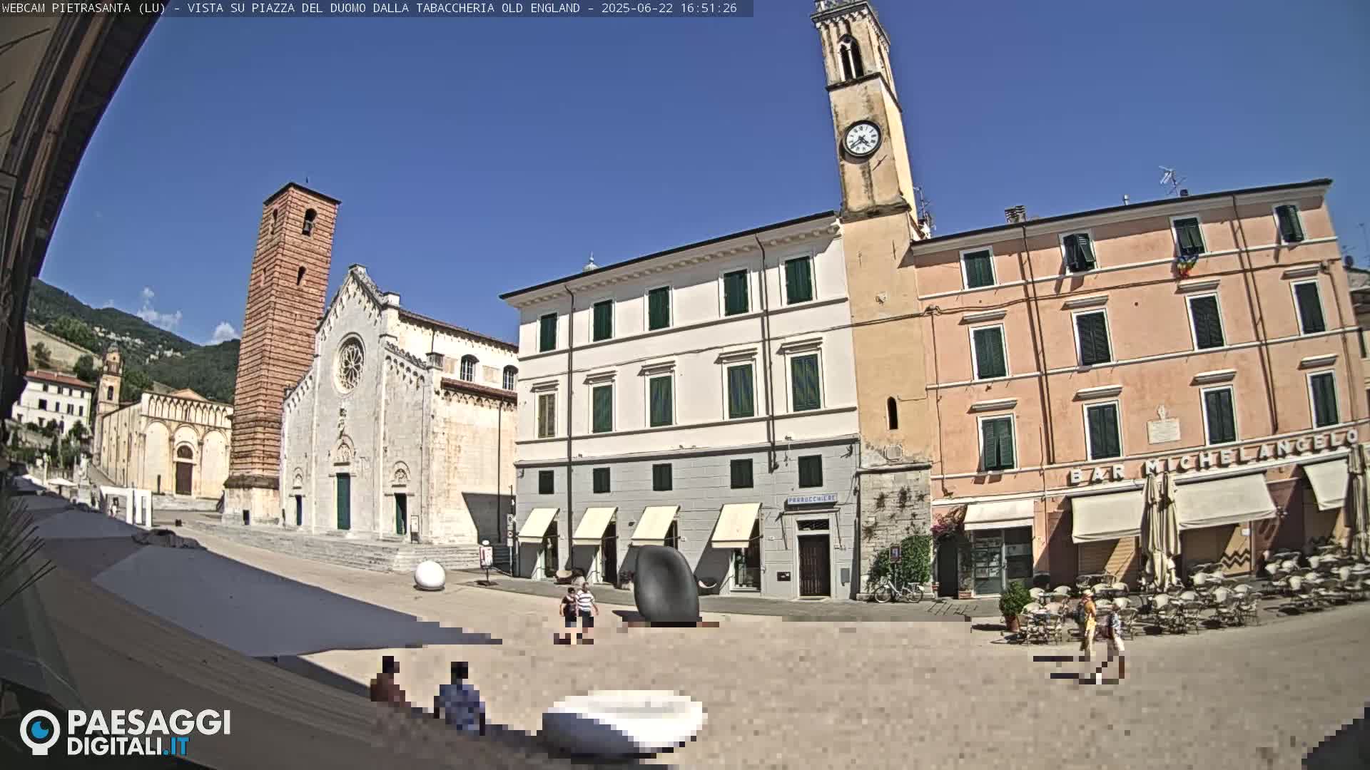 A sunny town square with a cathedral, clock tower, and several buildings, including a cafe, is shown.