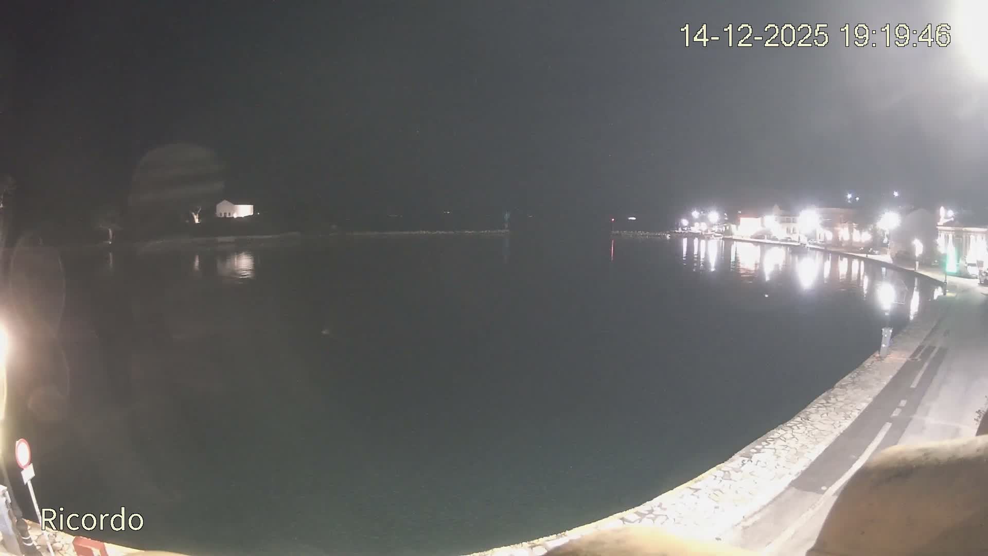 An overcast and rainy day is depicted over a tranquil coastal bay, featuring historic-looking buildings lining the waterfront, a distant point with a white building, and a person walking with an umbrella on a wet promenade.