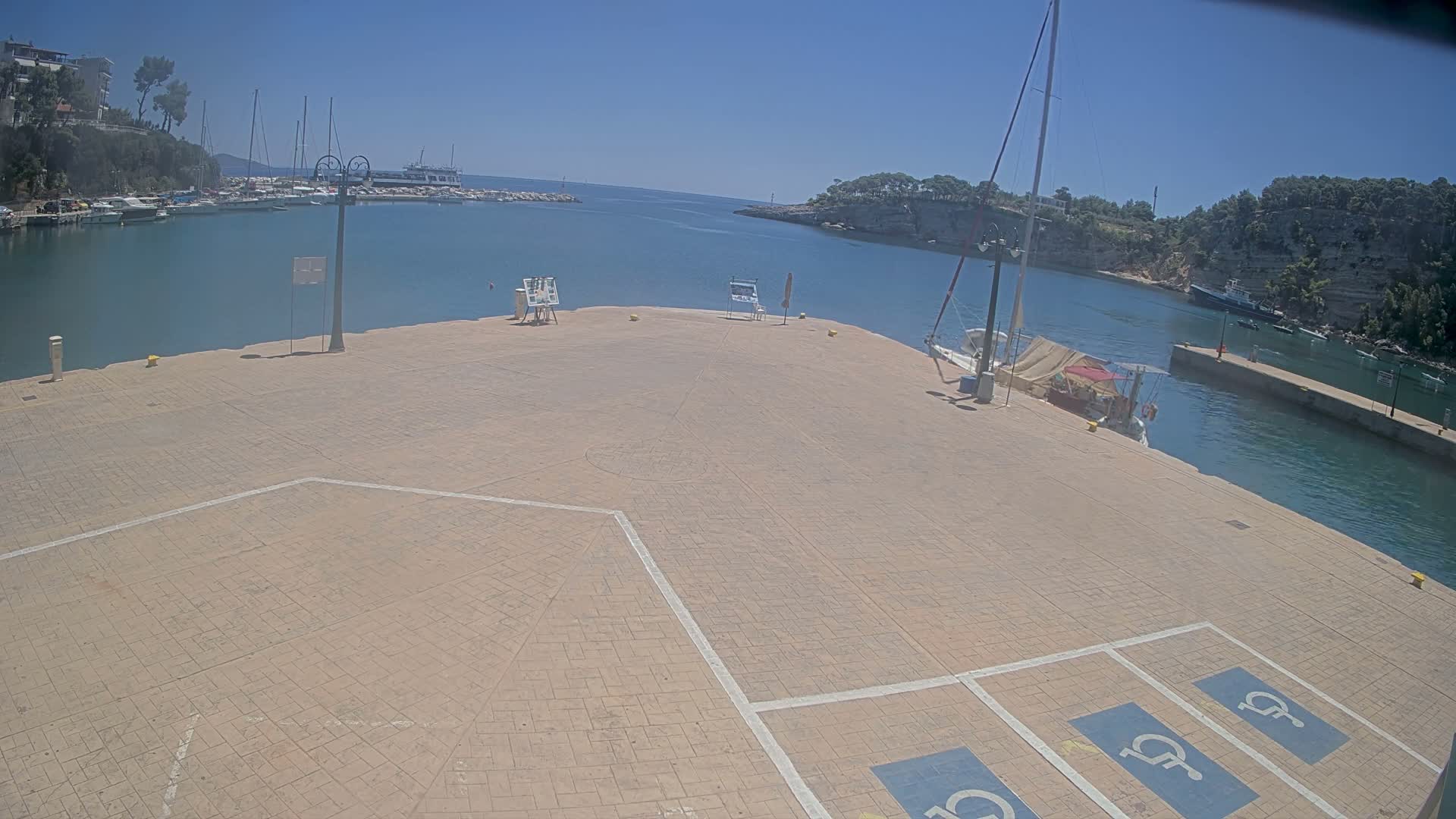 A paved plaza overlooks a calm harbor filled with boats on a sunny day.