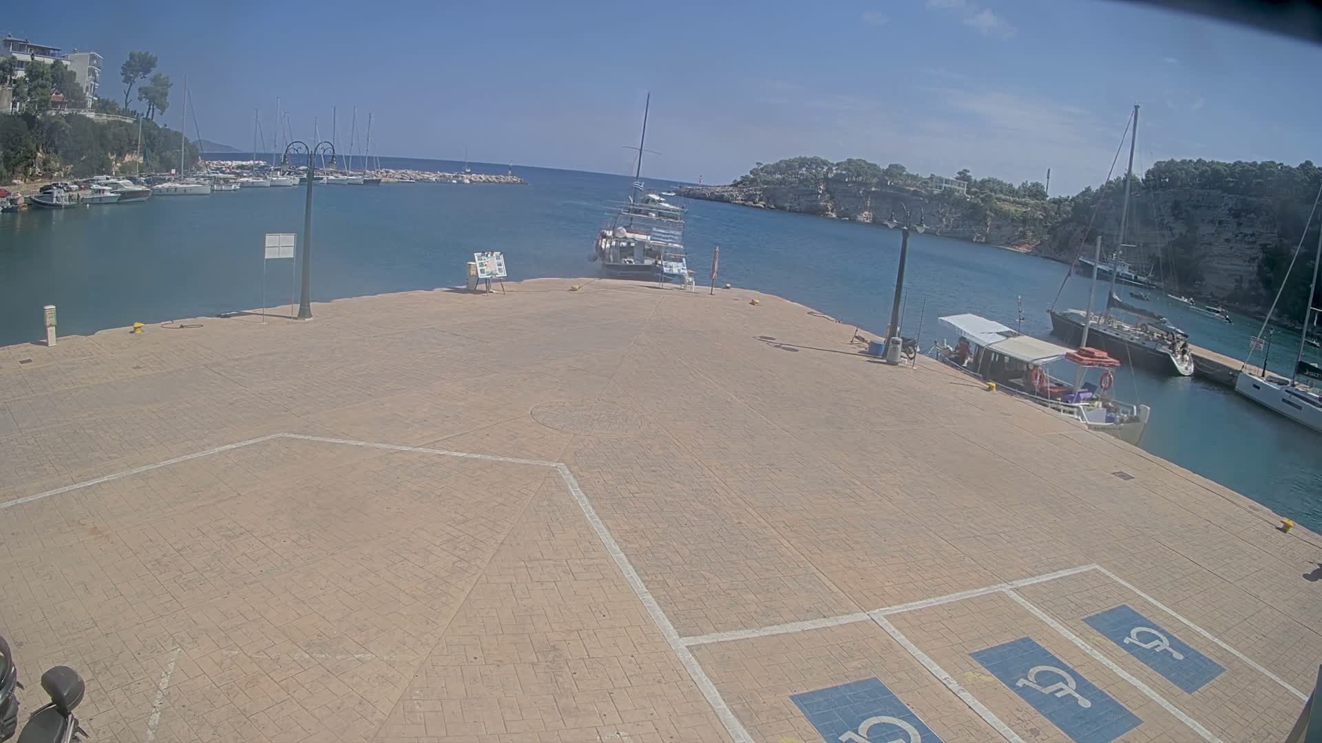 A paved area with several docked boats in a calm harbor under a partly cloudy sky.