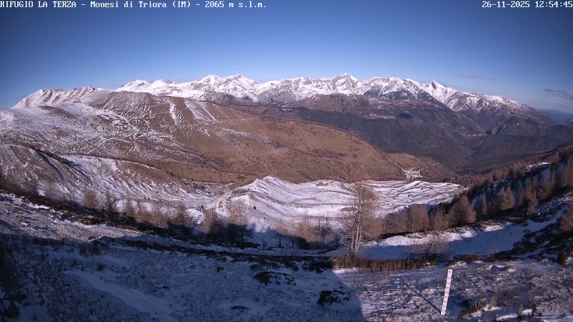 A snow-covered mountainous landscape appears muted under a heavy fog and overcast sky, with bare trees dotting the hillsides.